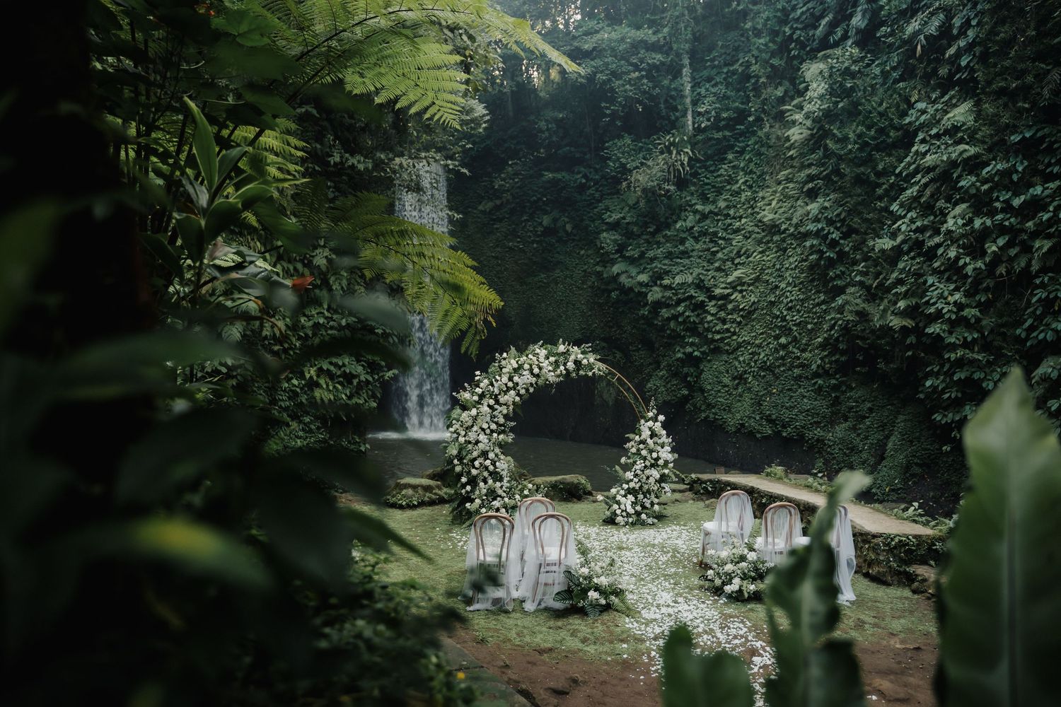 Lush jungle wedding ceremony setup with circular floral arch and waterfall backdrop in Bali.