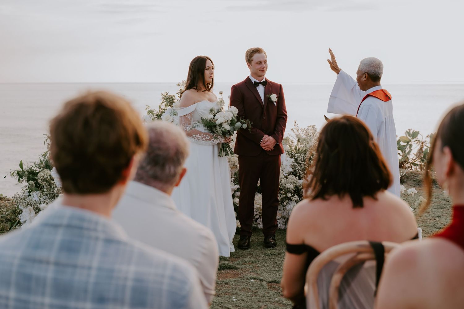 Bride and groom stand at the altar during an intimate outdoor oceanview wedding ceremony with guests seated.