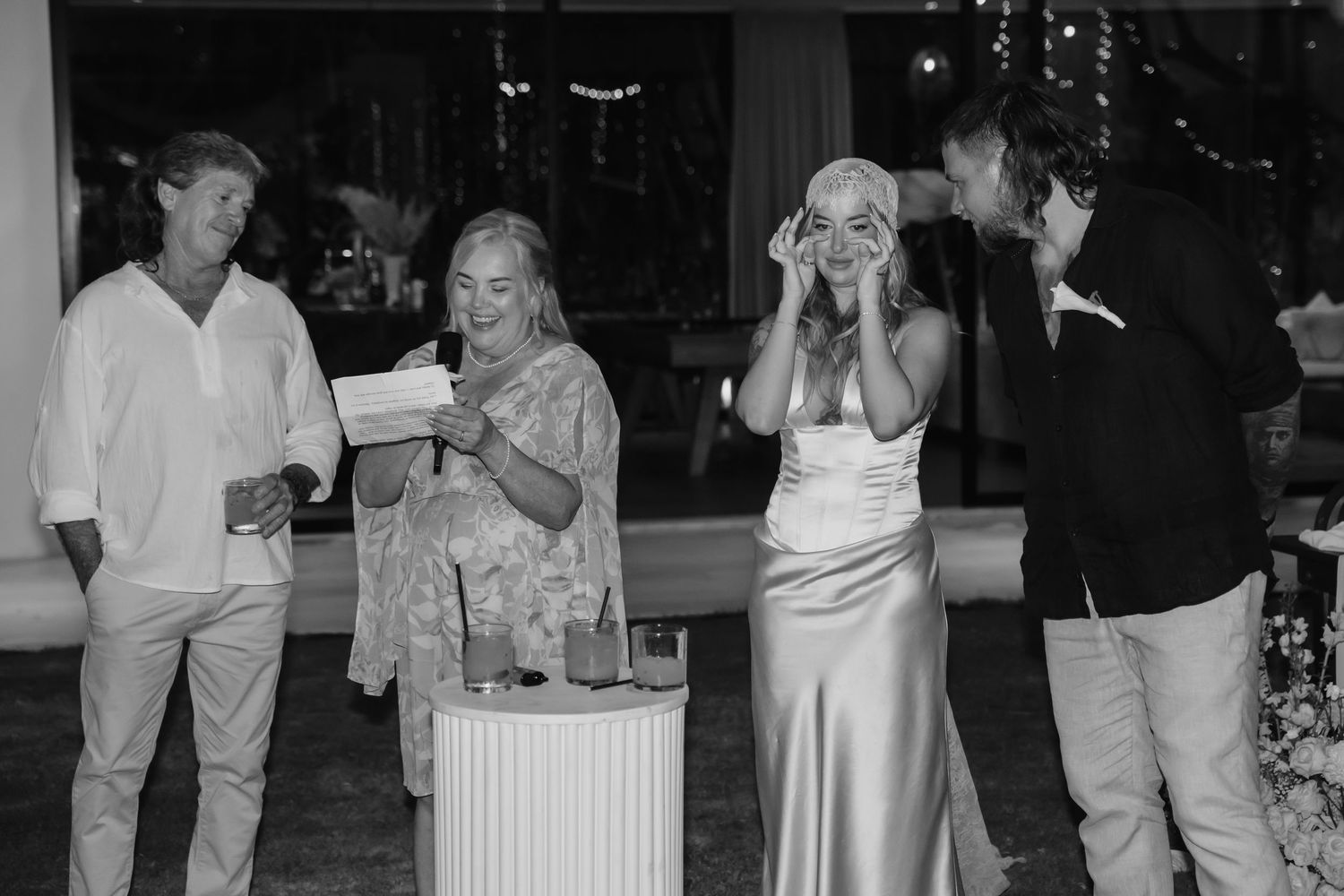Black and white photo of wedding guests reacting with joy and surprise during a heartfelt reception moment.