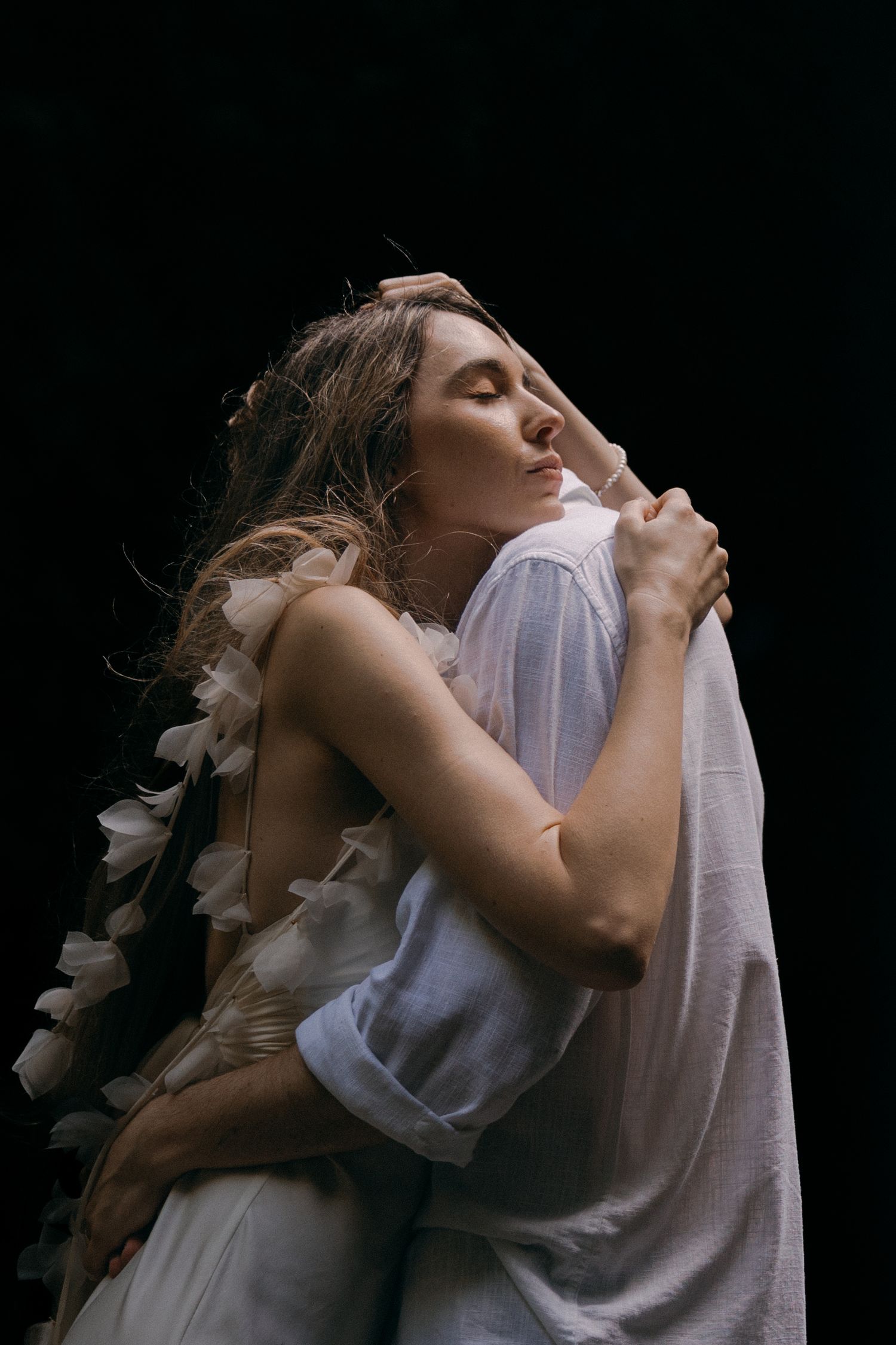 A person wearing a white shirt leans back with eyes closed against a dark background in an artistic portrait series.