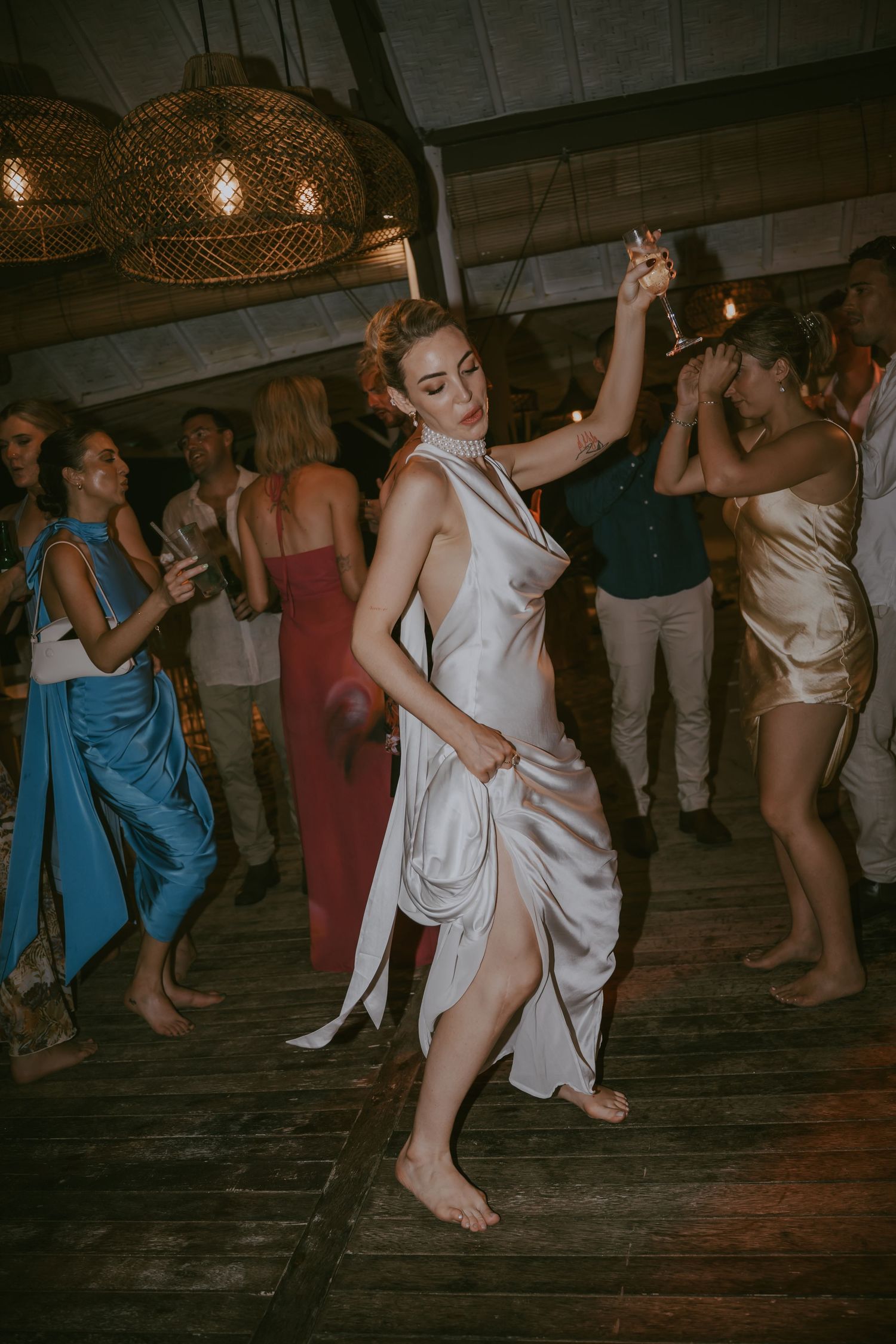 A dancer in a flowing white dress twirls gracefully on a wooden floor at a wedding reception.