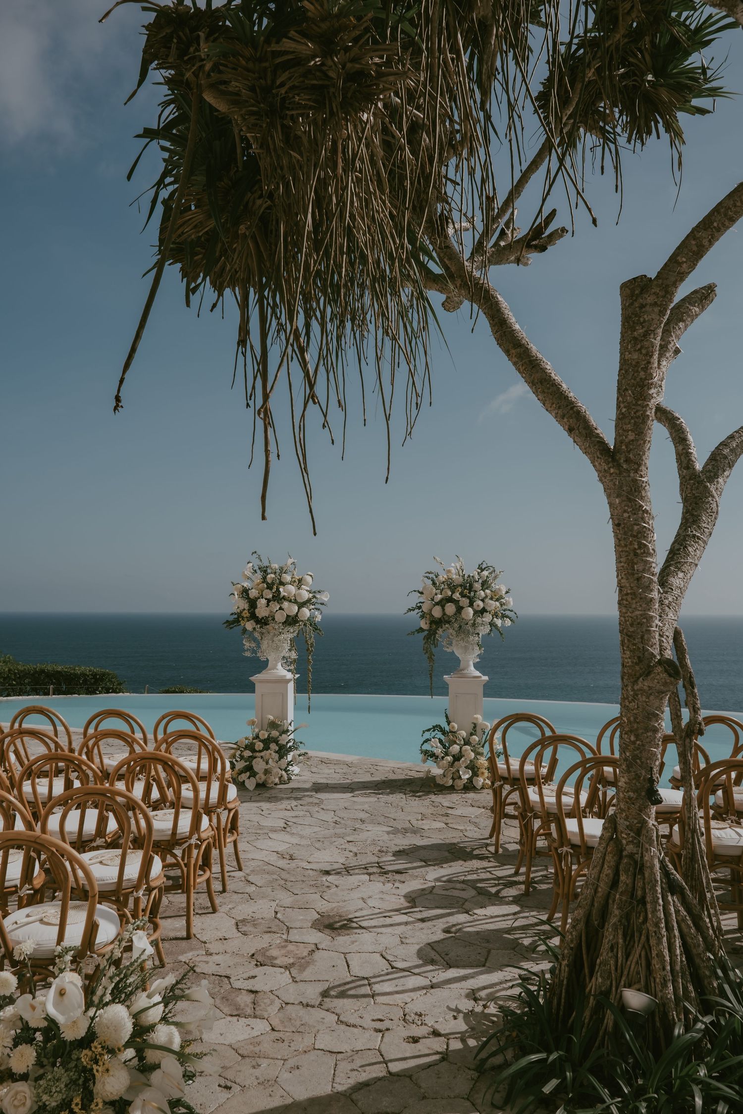 Oceanfront wedding ceremony setup with wooden chairs and palm trees against a blue horizon.