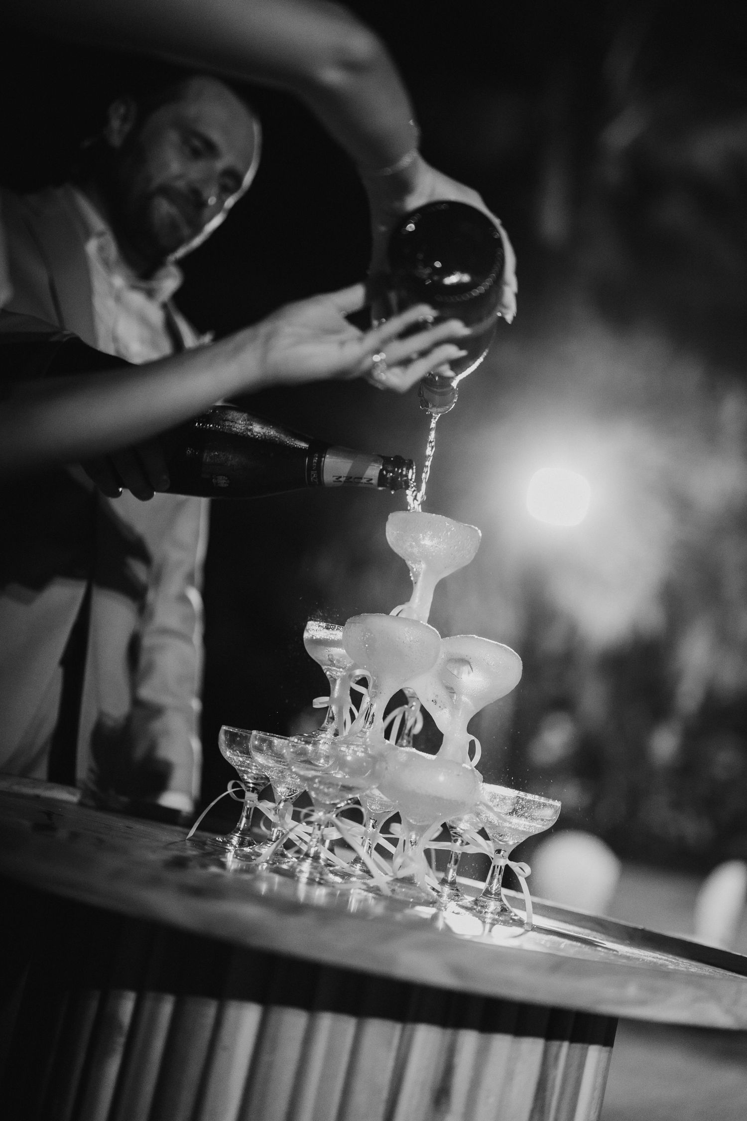 Black and white photo of a bartender pouring champagne over a classic champagne tower at a wedding.