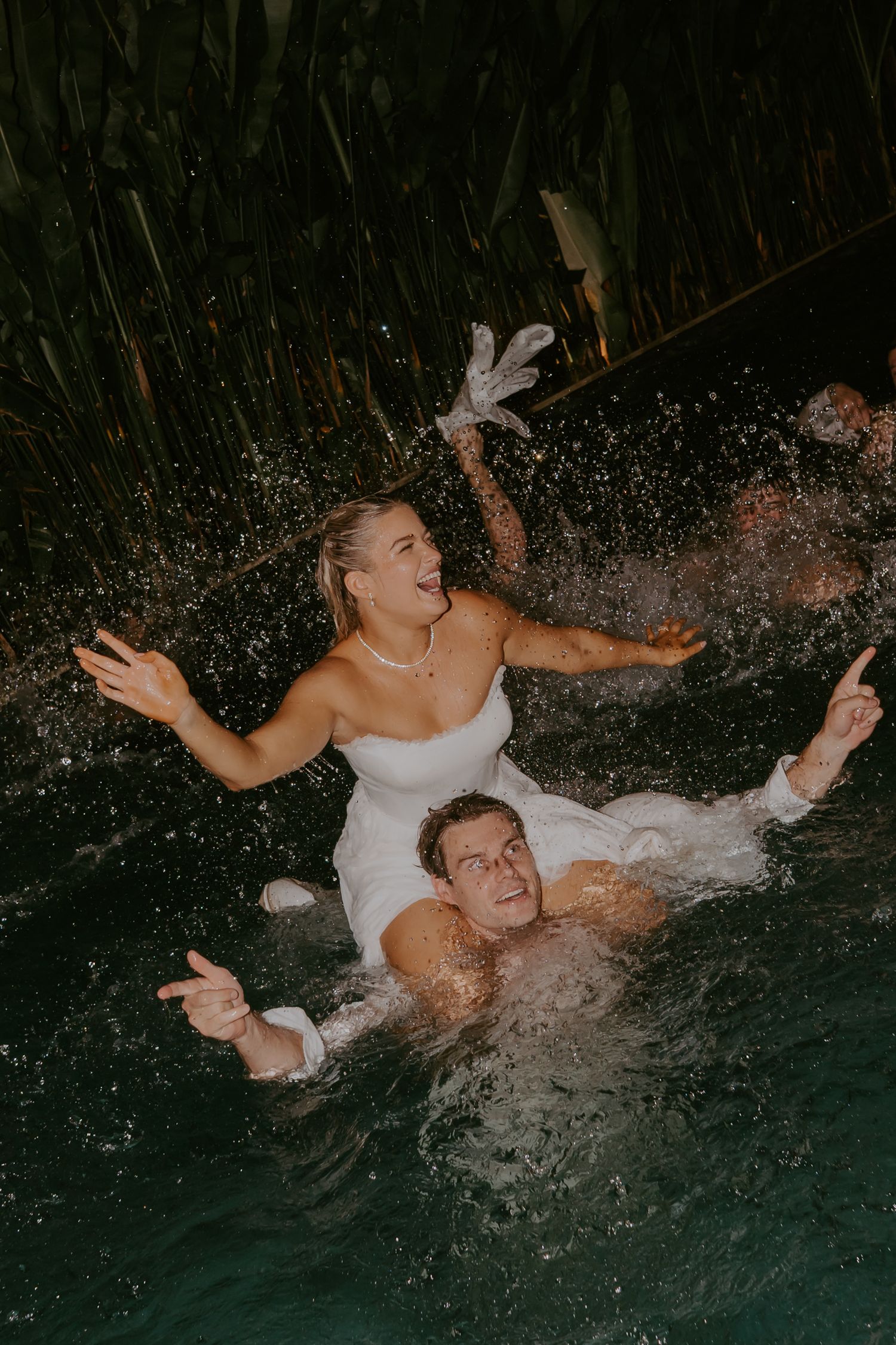 Bride and groom laughing as they splash together in pool at end of wedding night.