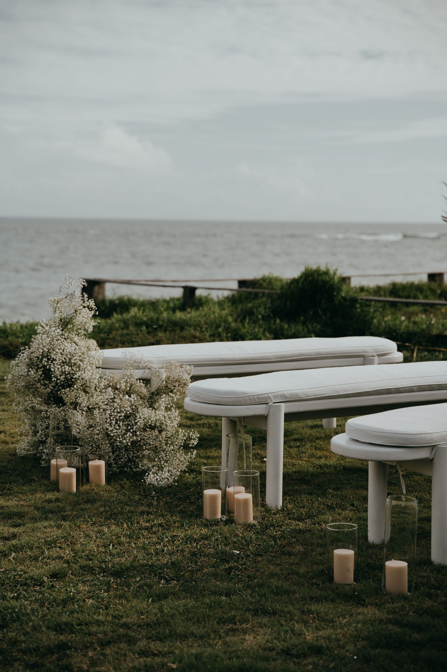 White wedding benches with baby's breath flowers and pillar candles beside the ocean.