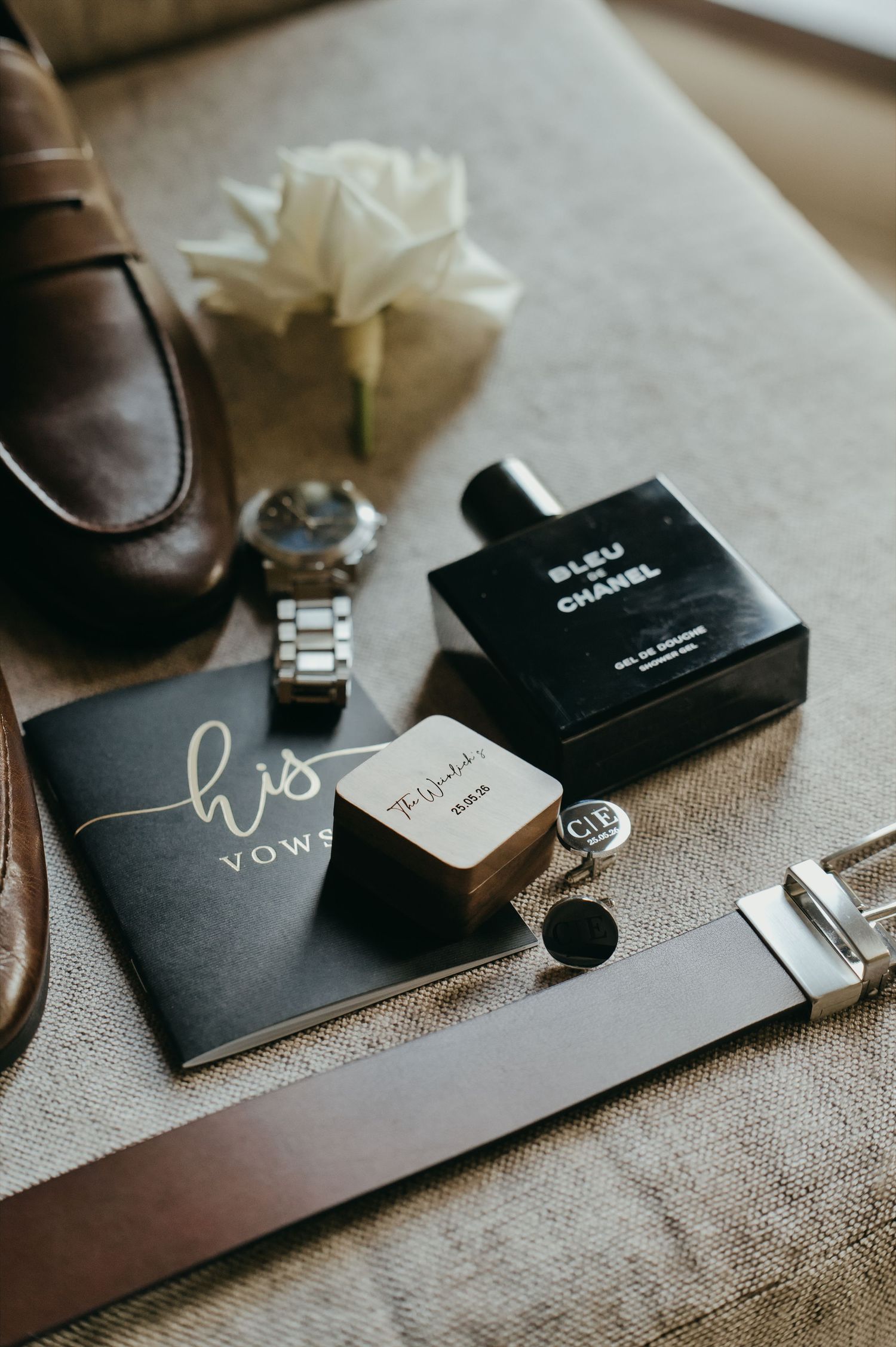 Groom wedding flat lay with vow book, Bleu de Chanel cologne, cufflinks, watch, and white rose boutonniere.
