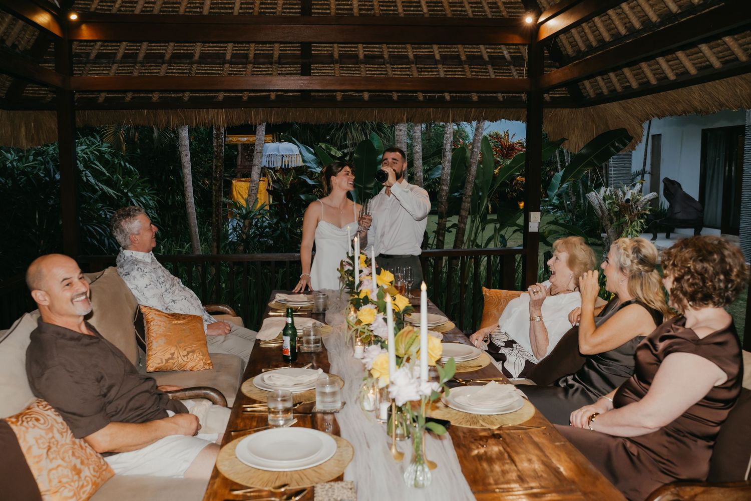 Wedding couple and guests gathered around a decorated dining table during an intimate outdoor reception.