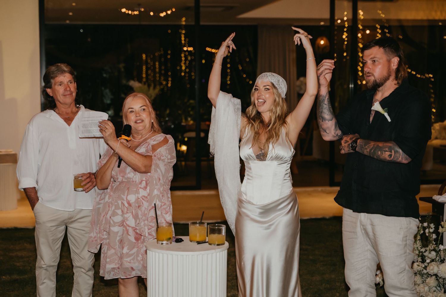 Bride in satin gown celebrates joyfully with wedding guests at evening reception.