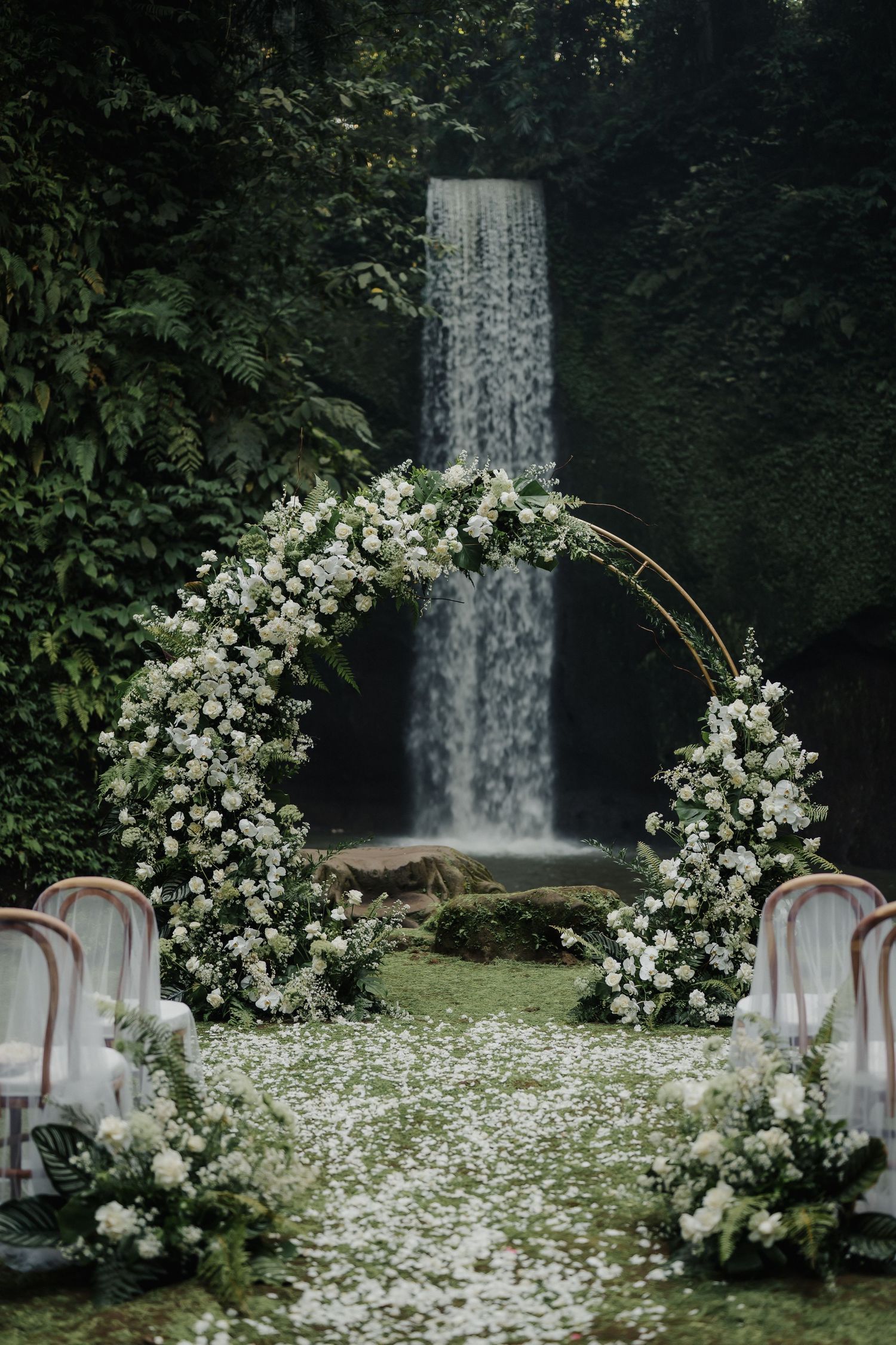 Elegant circular floral arch with white flowers frames a stunning waterfall wedding ceremony backdrop.