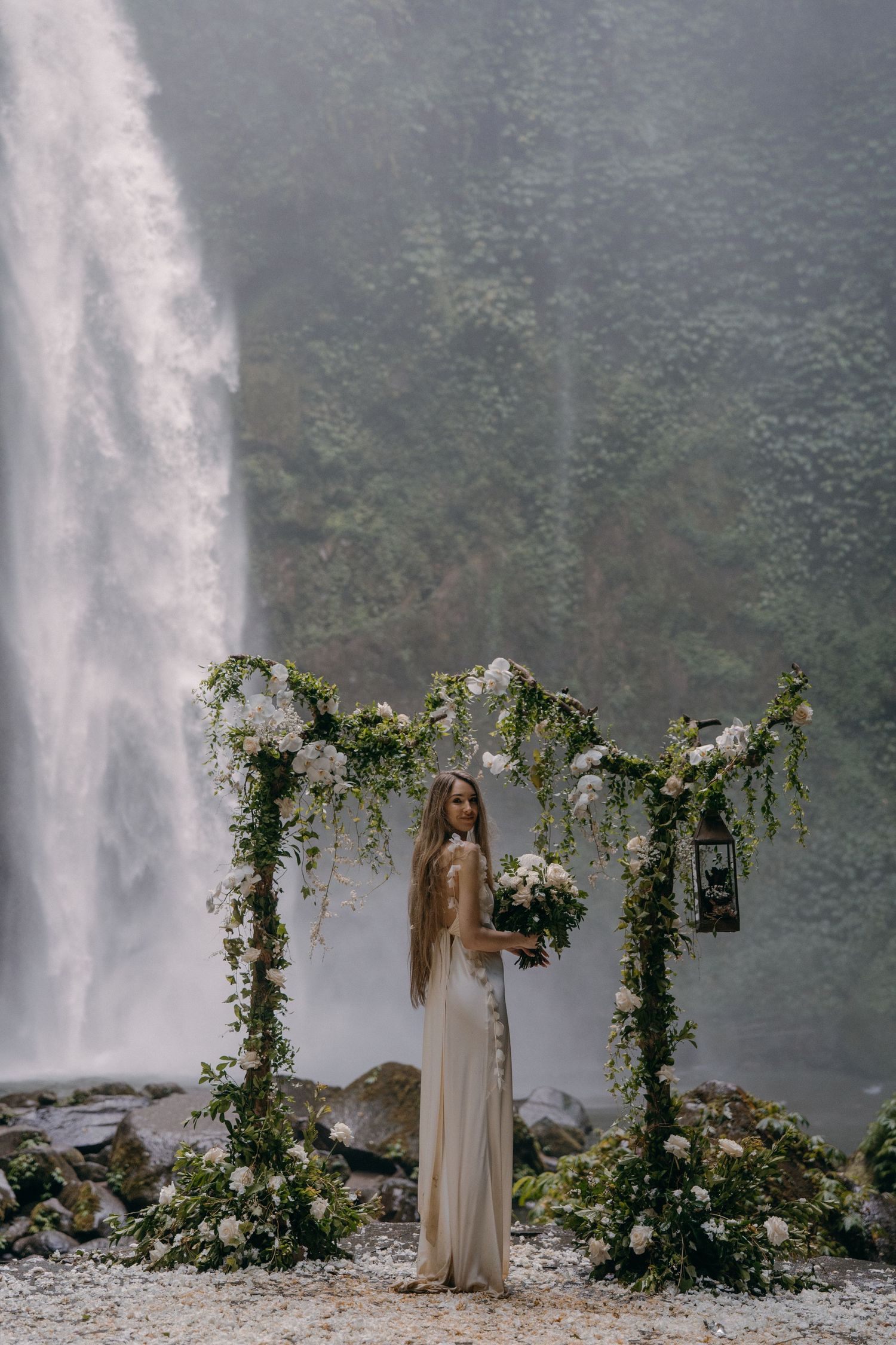 A floral wedding arch stands before a majestic waterfall, creating a dreamy natural backdrop for an ethereal ceremony.