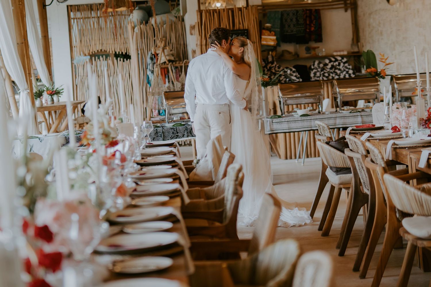 Bride and groom share intimate moment beside elegantly set long reception dinner table in boho venue.