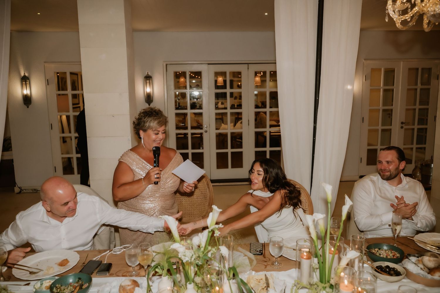 Wedding guest delivers heartfelt speech at elegant indoor reception dinner with floral centerpieces.