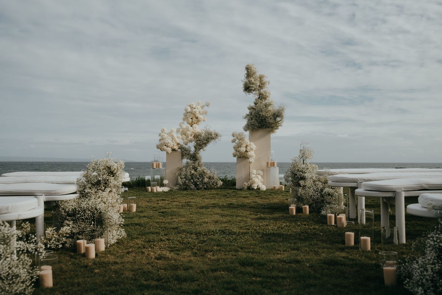 Elegant outdoor wedding ceremony setup with white floral arrangements and candles overlooking the ocean.