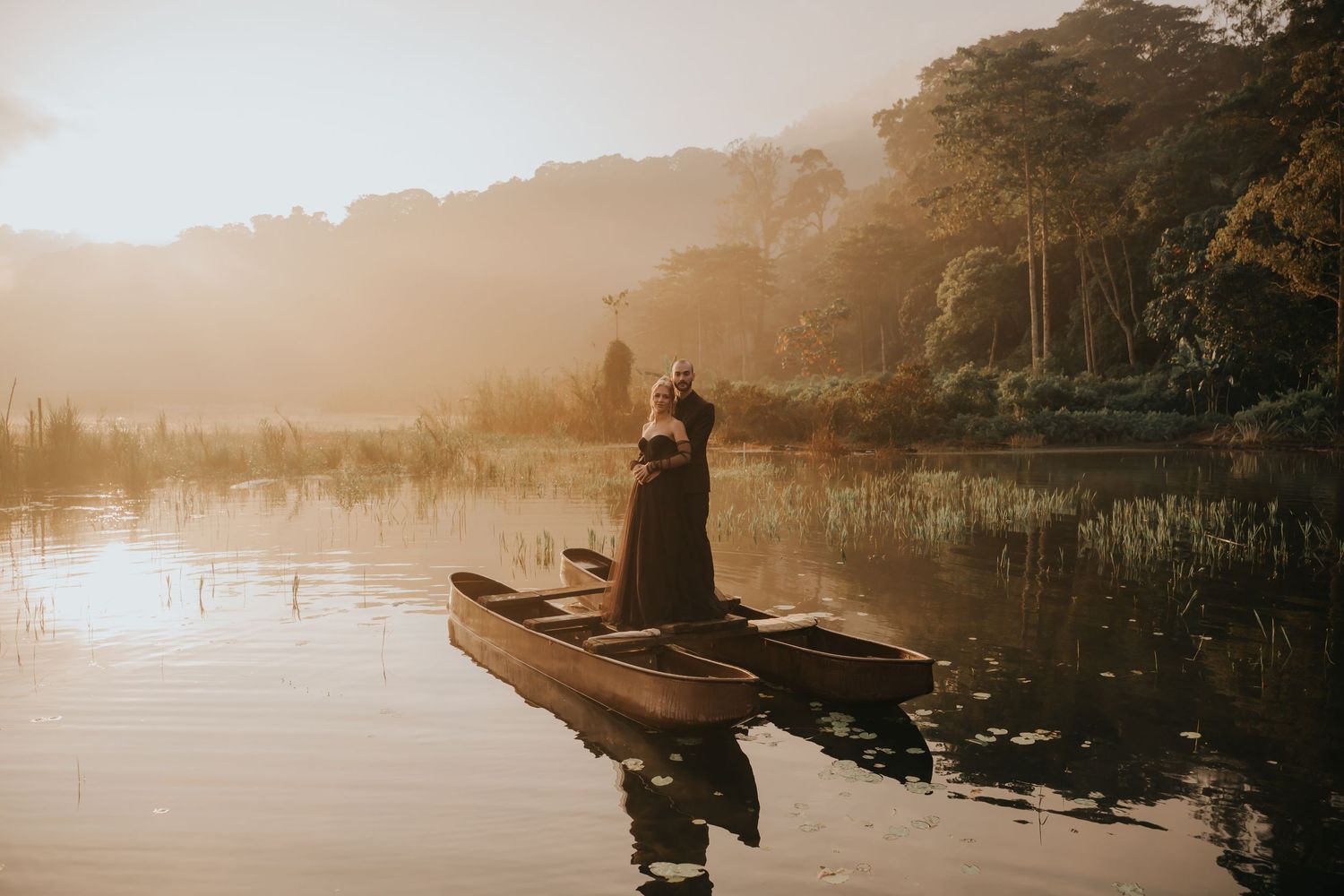 Panoramic view of a misty lake with silhouettes of people in boats during sunrise.