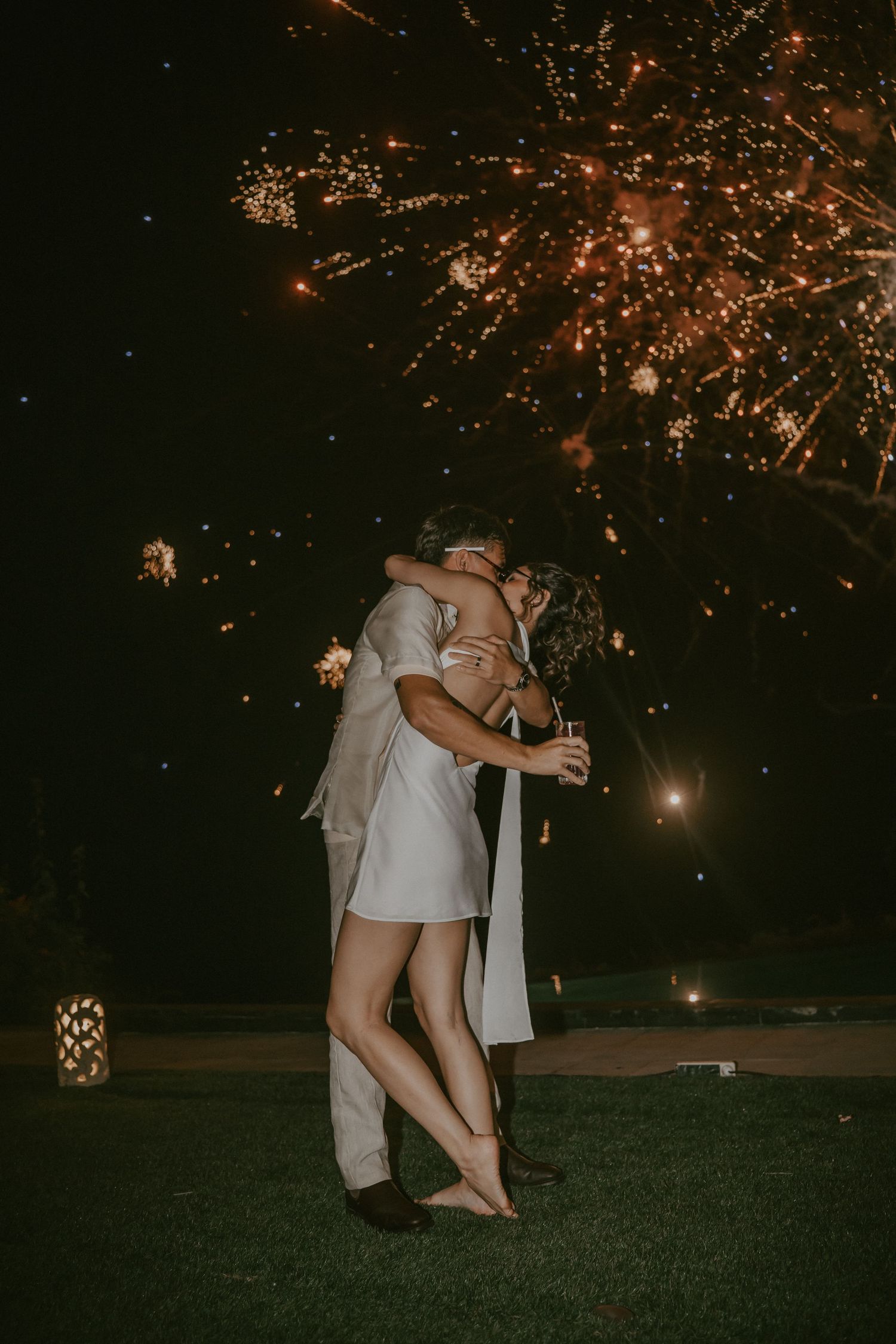 A couple embraces romantically at night with sparklers creating magical light trails in the background.
