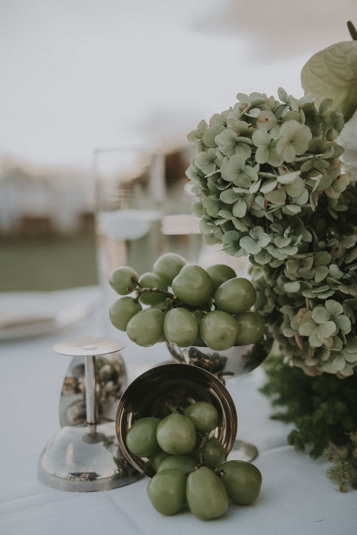 Green hydrangea flowers and fresh apples arranged on white table with decorative glass containers for elegant table setting.