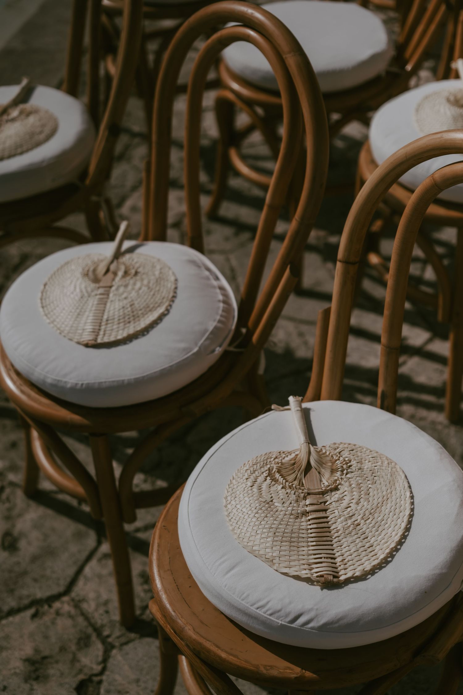 Rustic wooden chairs with white cushions arranged in rows for an outdoor event.