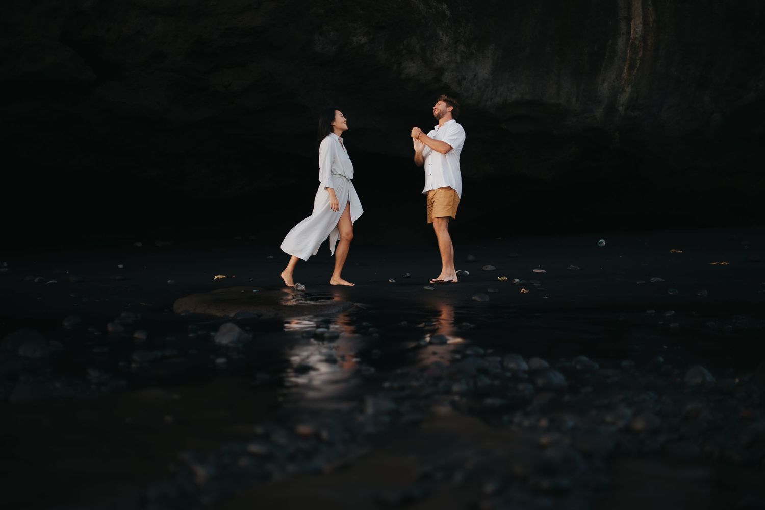 Two people stand in dark water at night creating ripples and reflections in the moonlight.