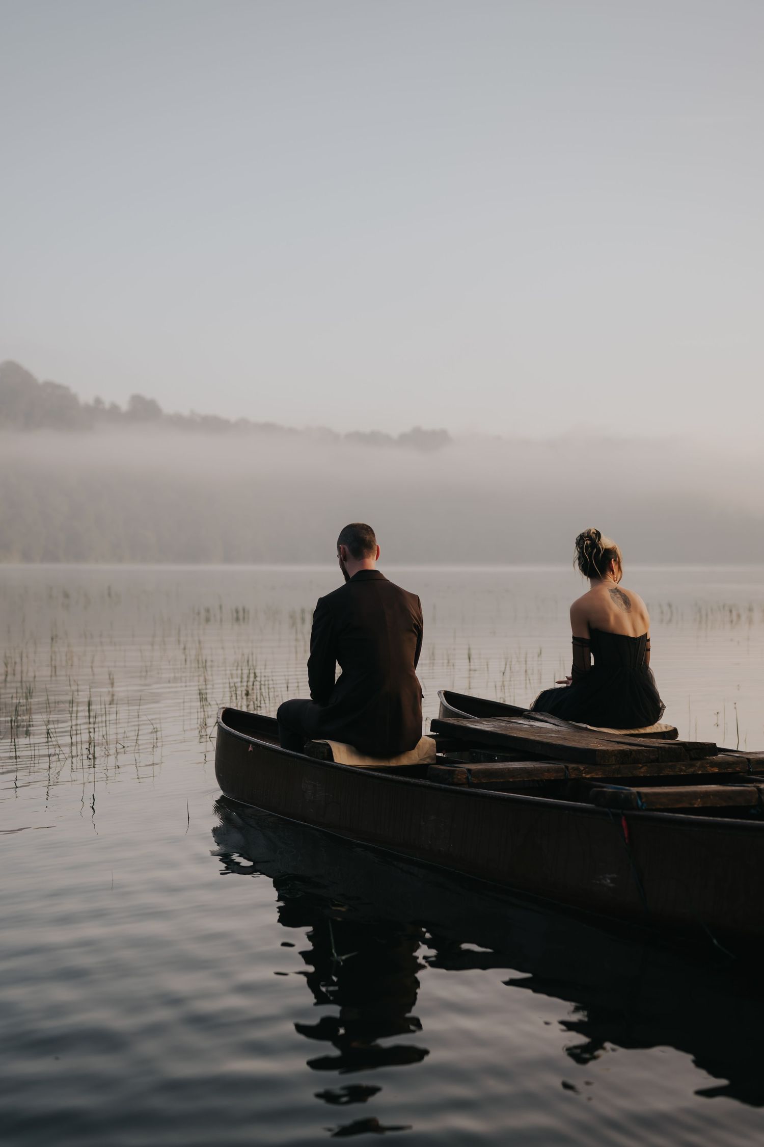 Two people sit together in canoes on a misty lake at dawn surrounded by calm waters.