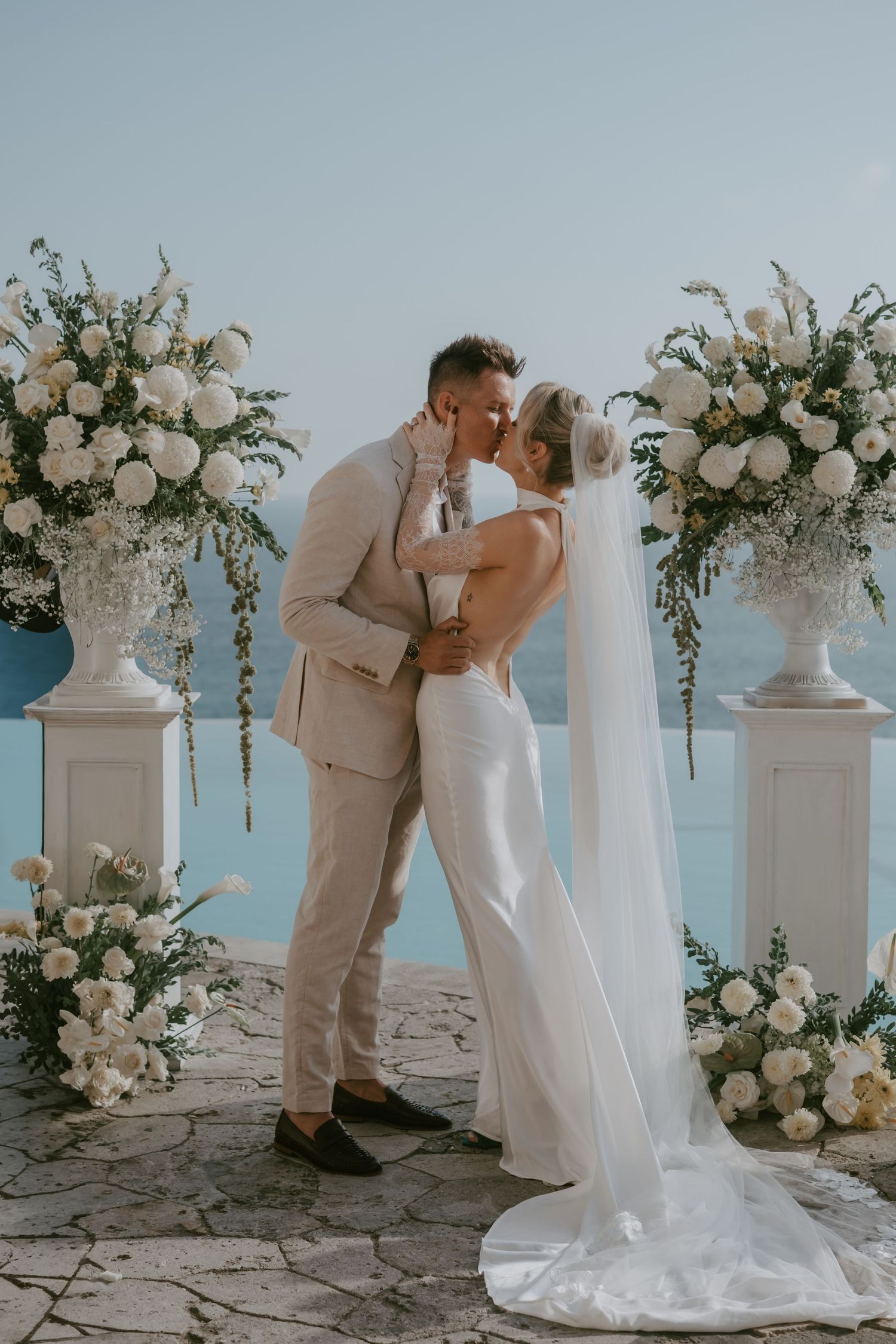 Romantic wedding ceremony moments captured against a seaside backdrop with elegant white floral decor.