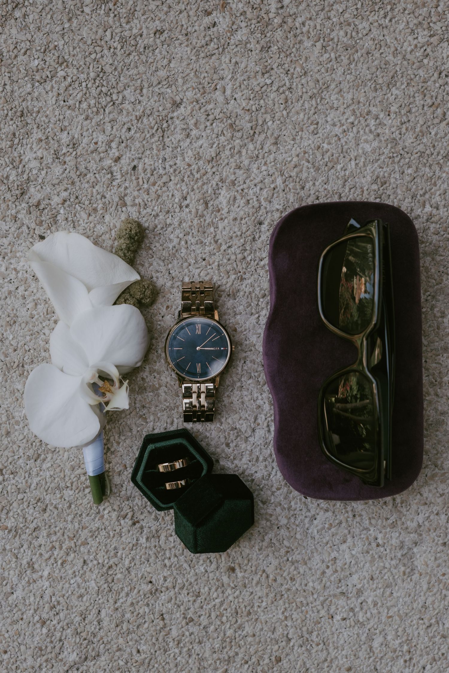 Wedding accessories including jewelry boxes, watches and delicate white details arranged on grey carpet.