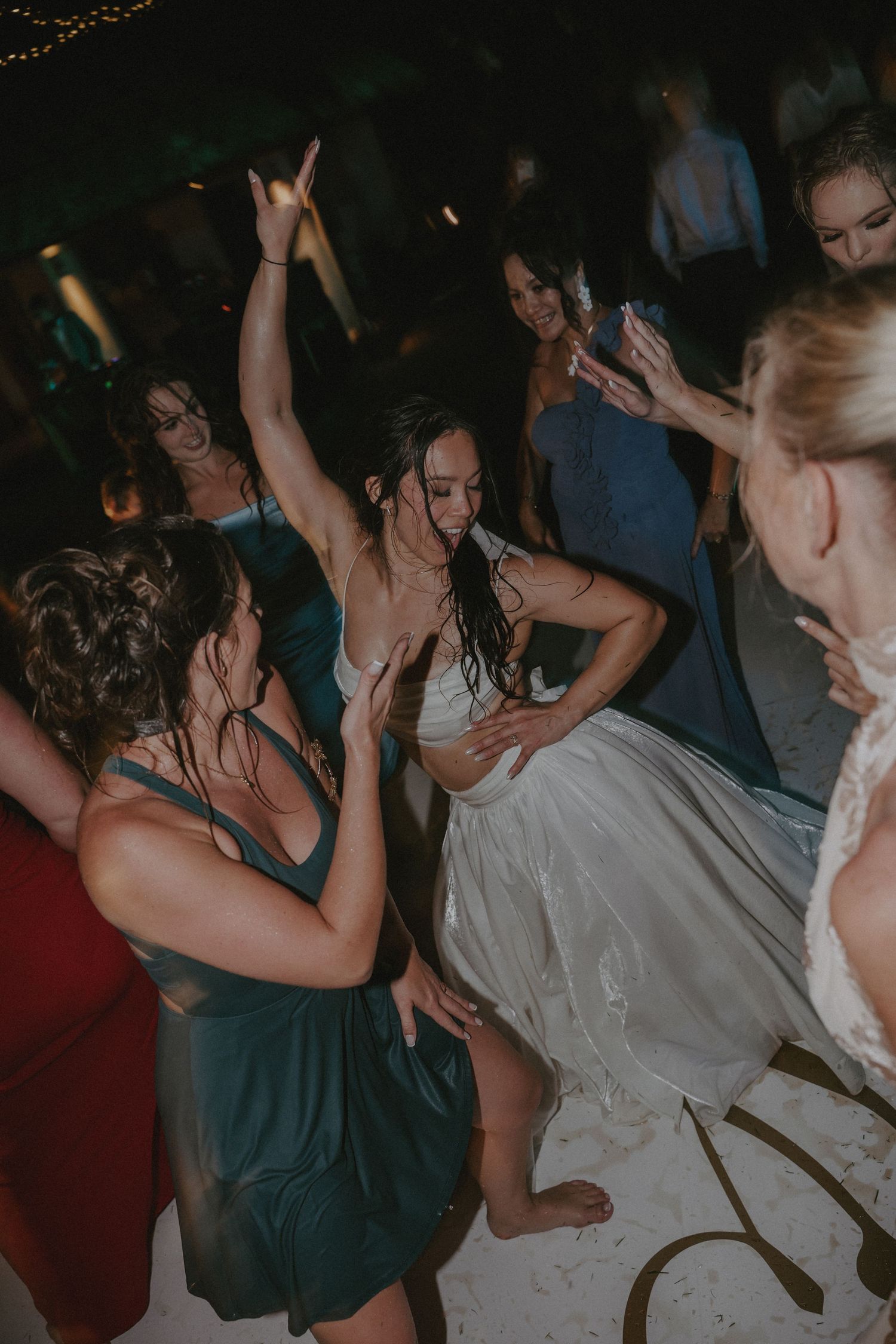 People dancing and celebrating at a lively party or wedding reception in a dimly lit venue.