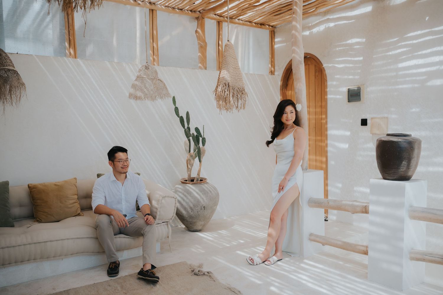 Couple posing in a modern Bali-inspired interior with white walls, rattan decor, cactus, and natural textures.