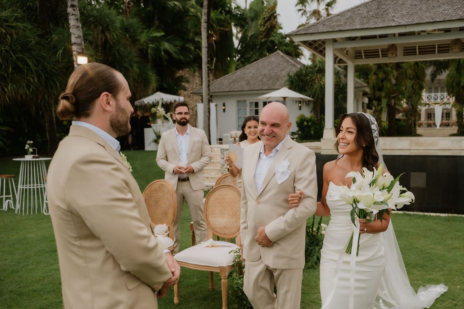 Father of the bride escorting smiling bride to meet groom at outdoor garden wedding ceremony.