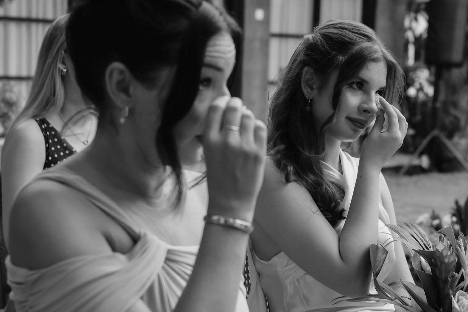 Black and white photo of two women wiping tears at a wedding ceremony, showing emotional moment.