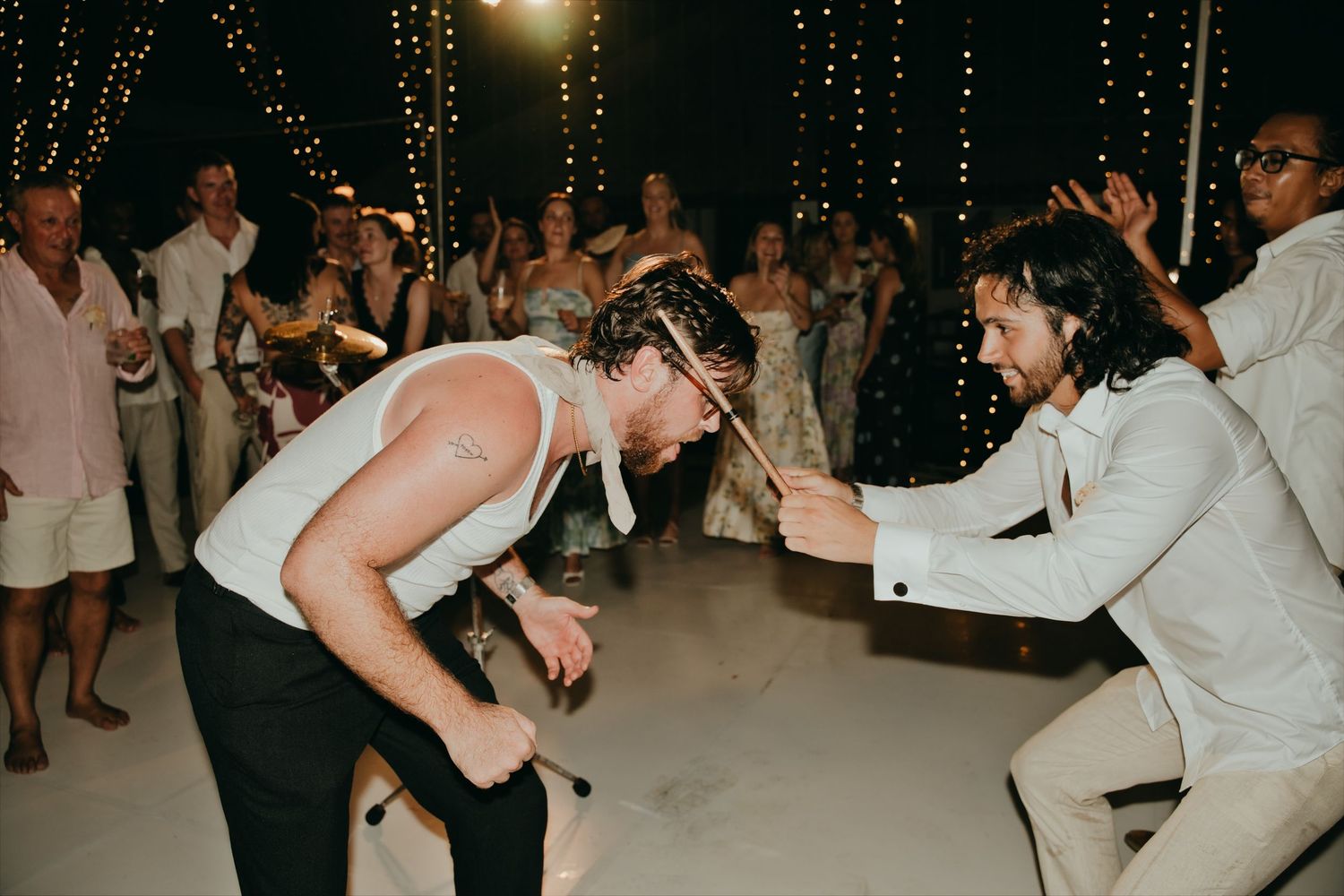 Guests energetically dancing and playing air guitar on white dance floor at outdoor wedding reception.