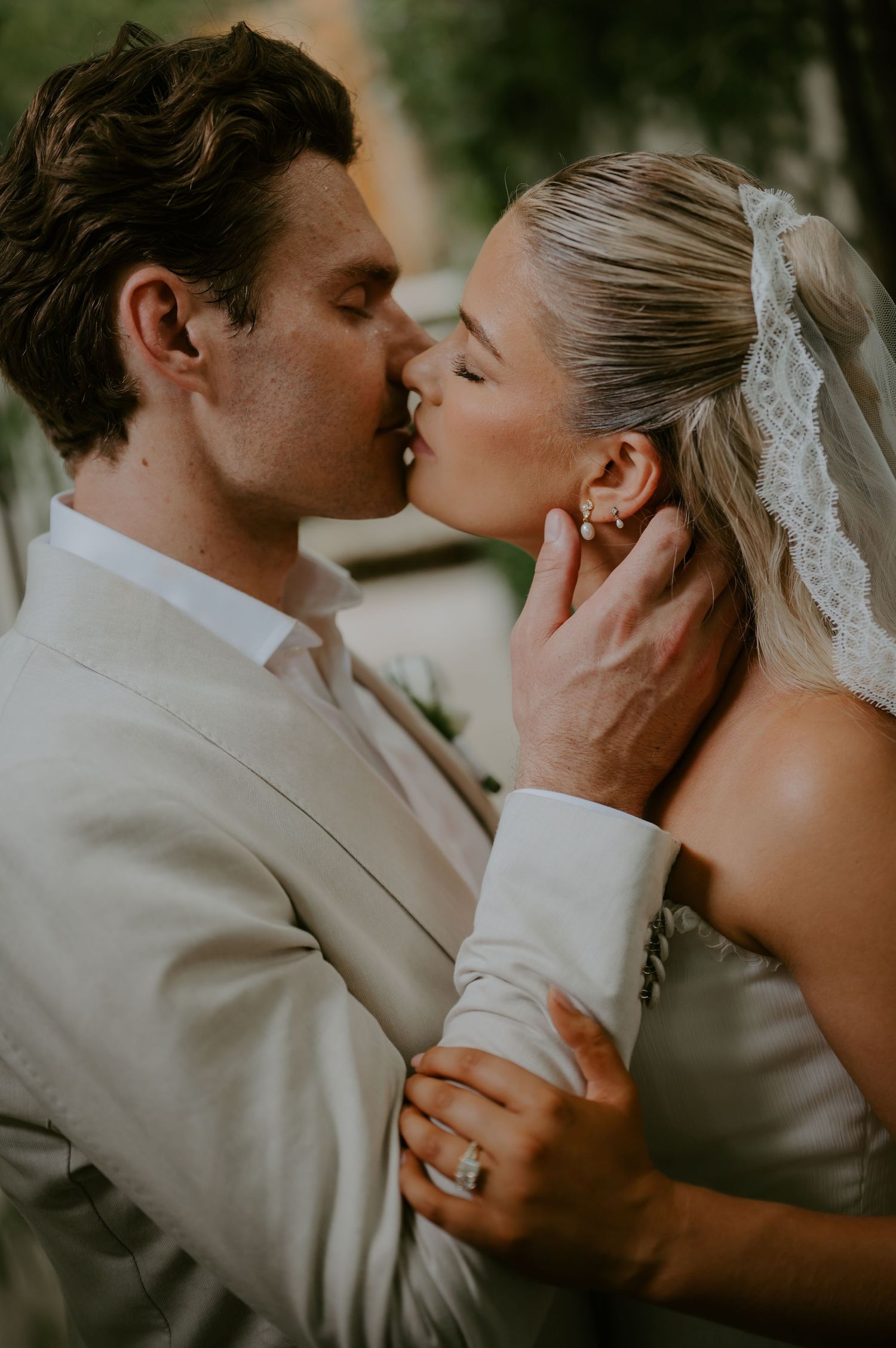 Bride and groom sharing a romantic first kiss, bride wearing lace veil and groom in beige suit.