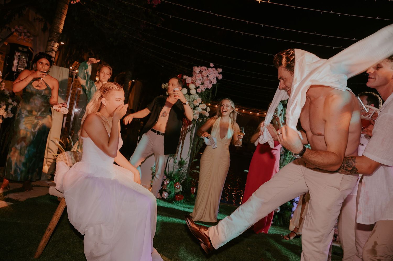 Energetic wedding guests dancing wildly with the bride and groom at a lively outdoor tropical reception at night.
