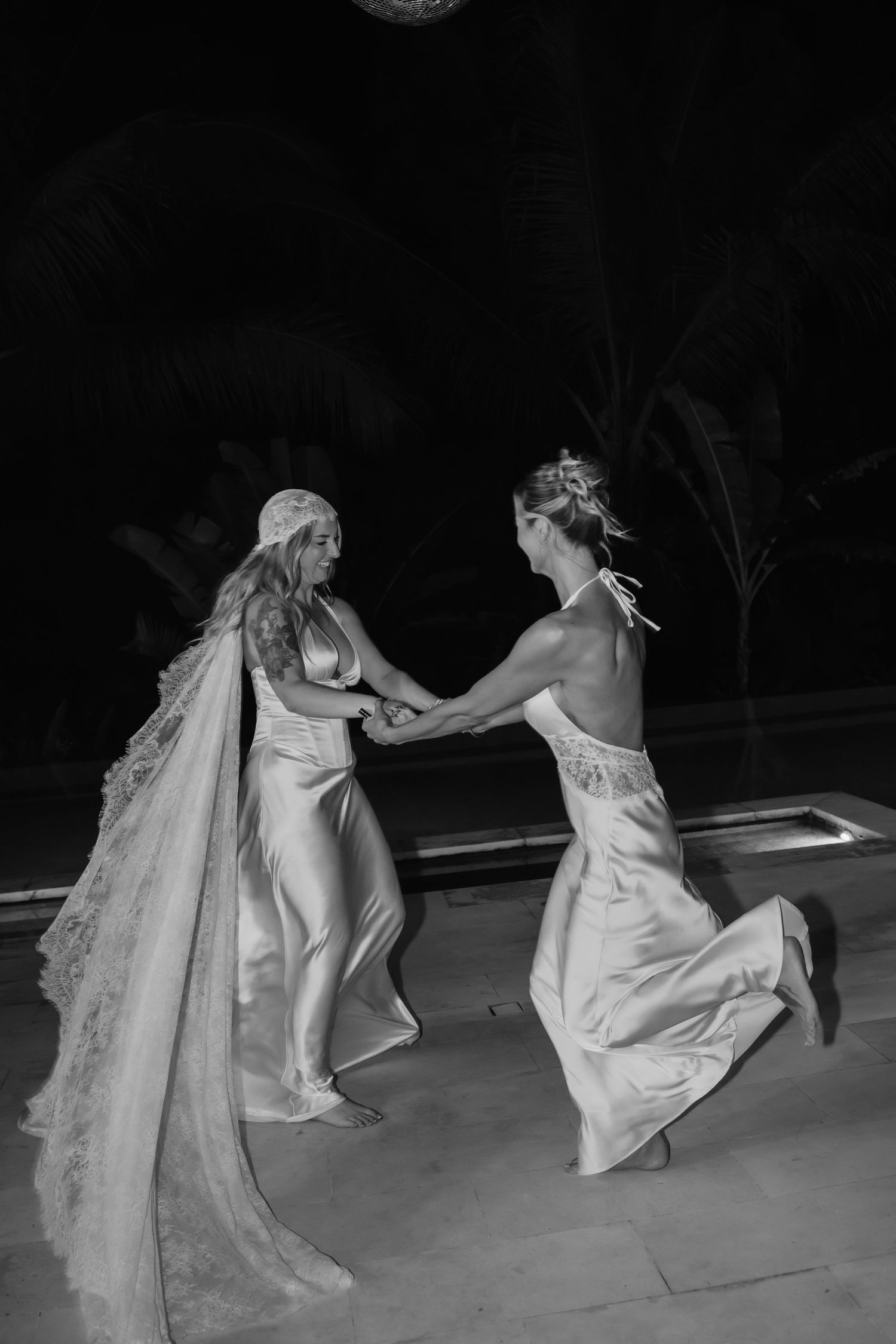 Black and white photo of two women in wedding gowns dancing together at night.