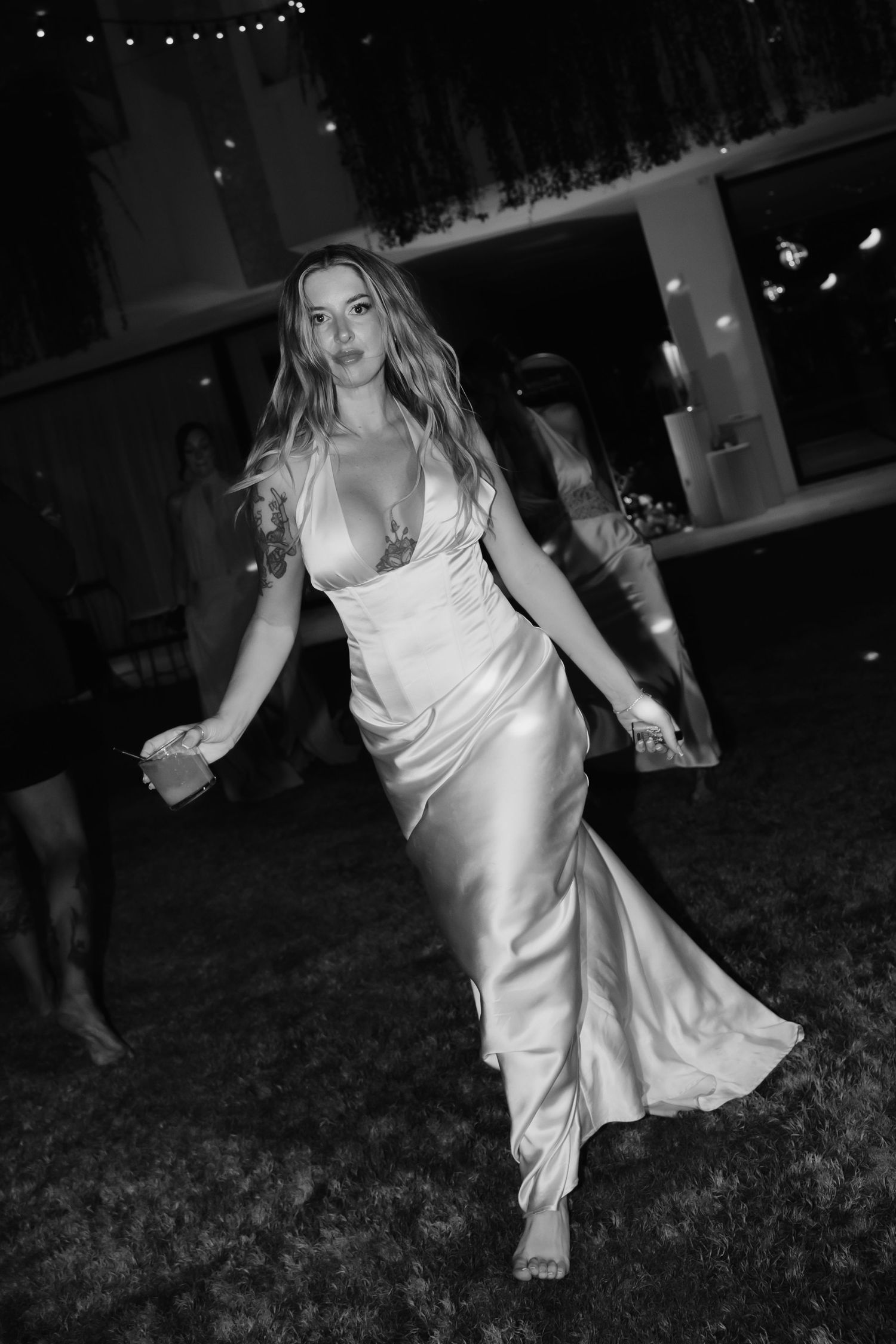 Black and white photo of bride in satin slip gown dancing confidently at outdoor wedding reception.