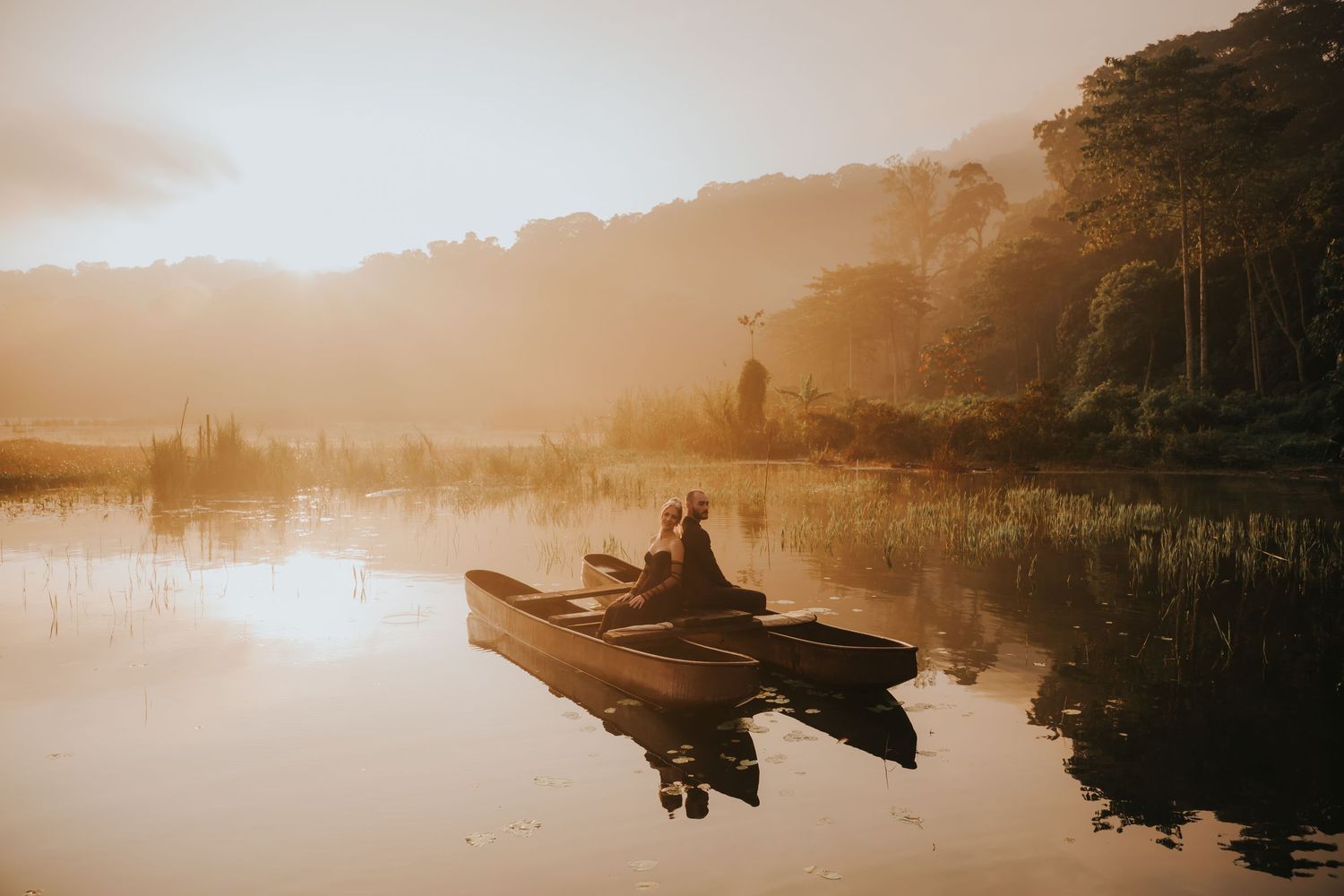 A peaceful lake at sunrise with a small boat silhouetted against the misty golden light reflecting on calm waters.