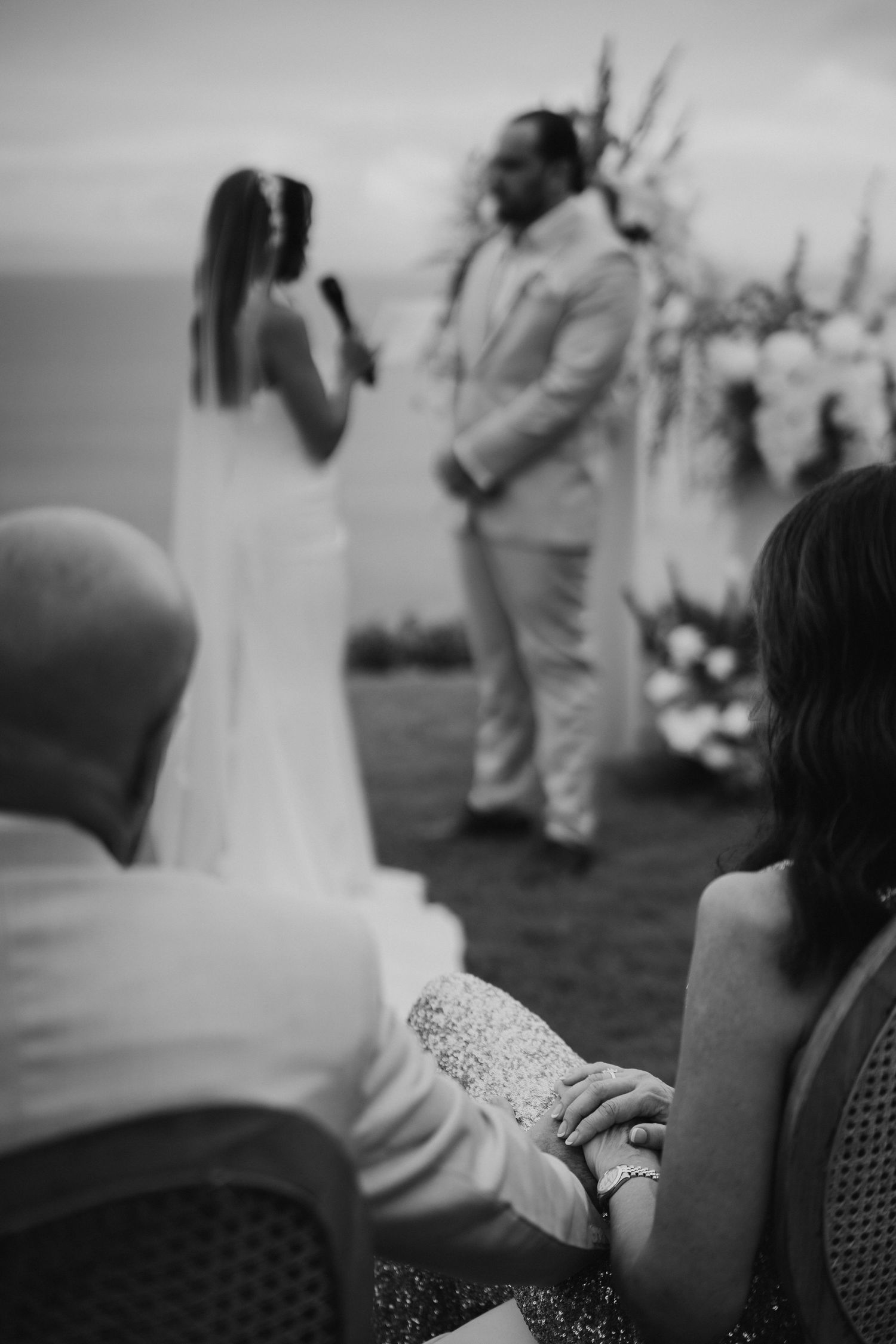 Black and white photo of an intimate outdoor wedding ceremony overlooking the ocean at sunset.