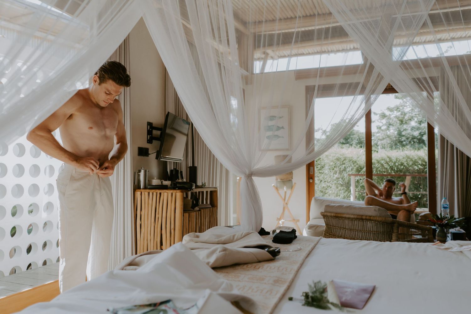 Man wrapping towel in a serene tropical villa bedroom with white canopy drapes and natural wood decor.