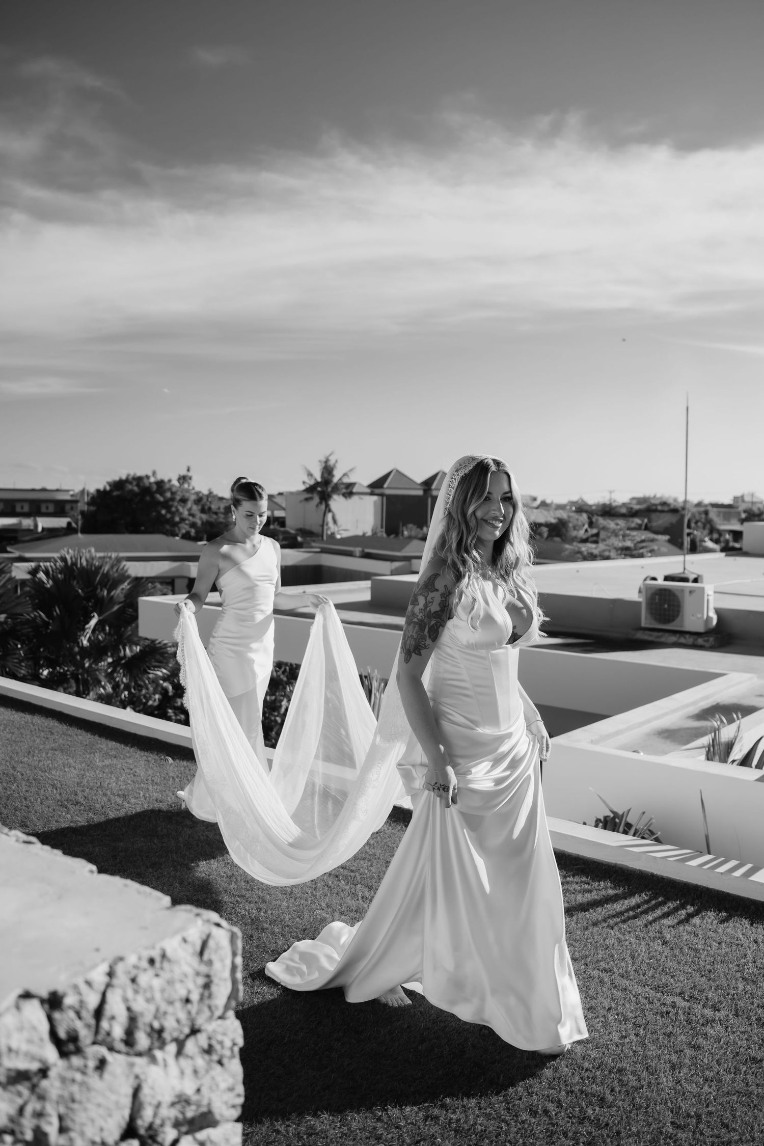 Black and white photo of a bride in a flowing gown and veil walking on a rooftop on her wedding day.