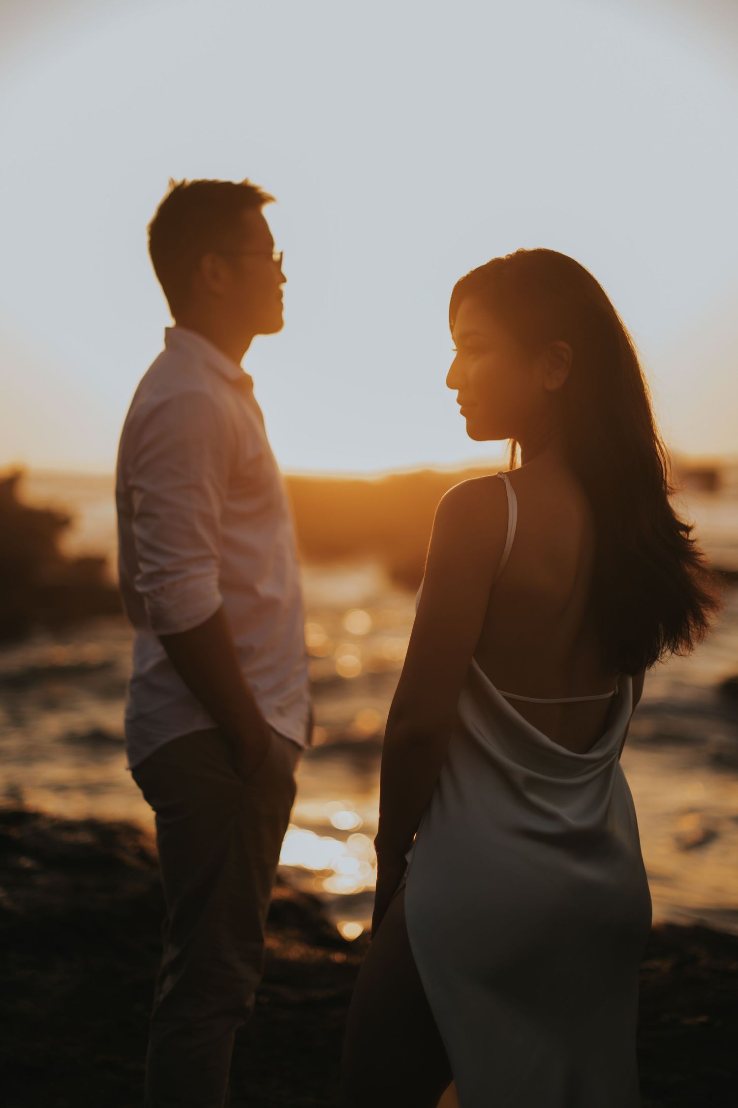 Couple sharing a romantic moment at sunset by the ocean, silhouetted against golden light.