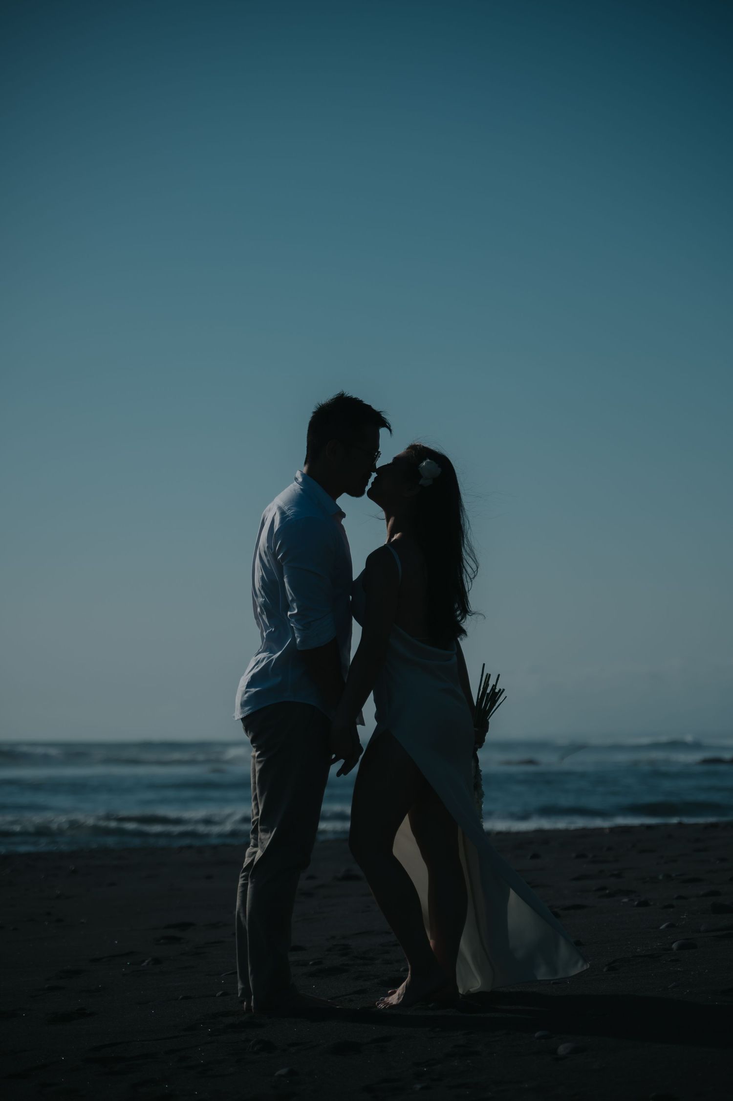 Romantic couple silhouette sharing an intimate moment on a beach at dusk with ocean waves in the background.