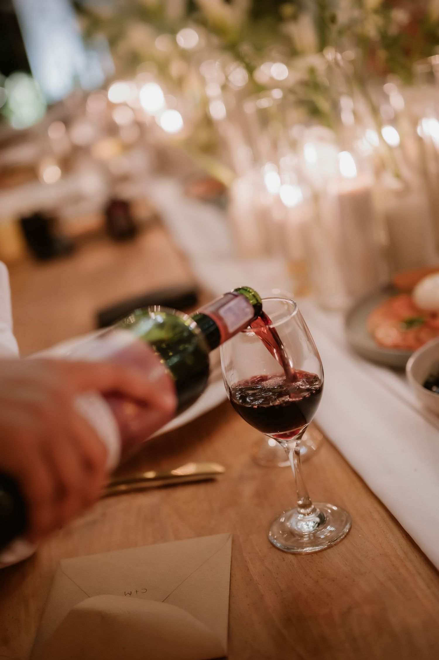 Red wine being poured into glass at elegantly set wedding reception dinner table.