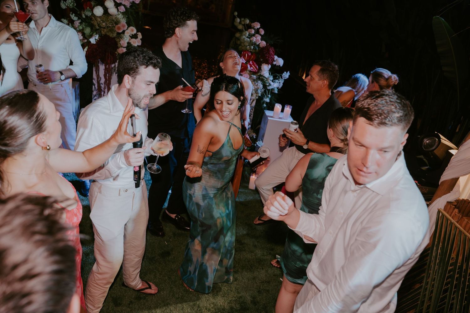 Wedding guests dancing and mingling on outdoor grass dance floor during evening tropical wedding reception.