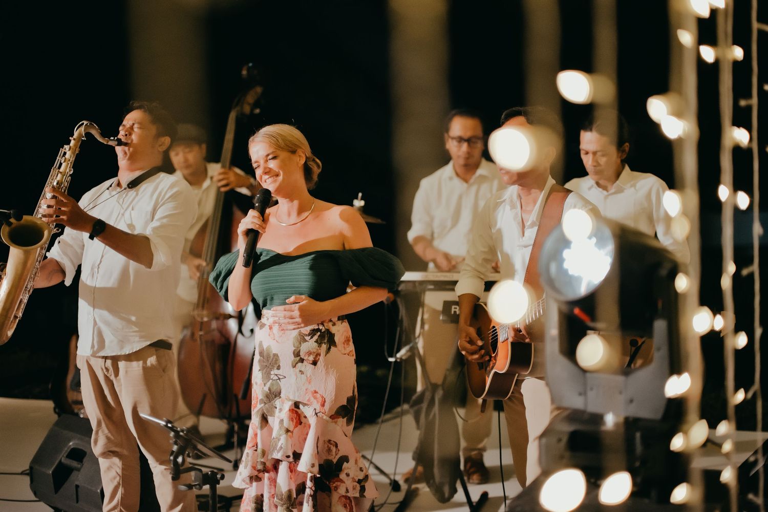 Live jazz band performs with female vocalist in floral skirt at elegant outdoor evening wedding reception.