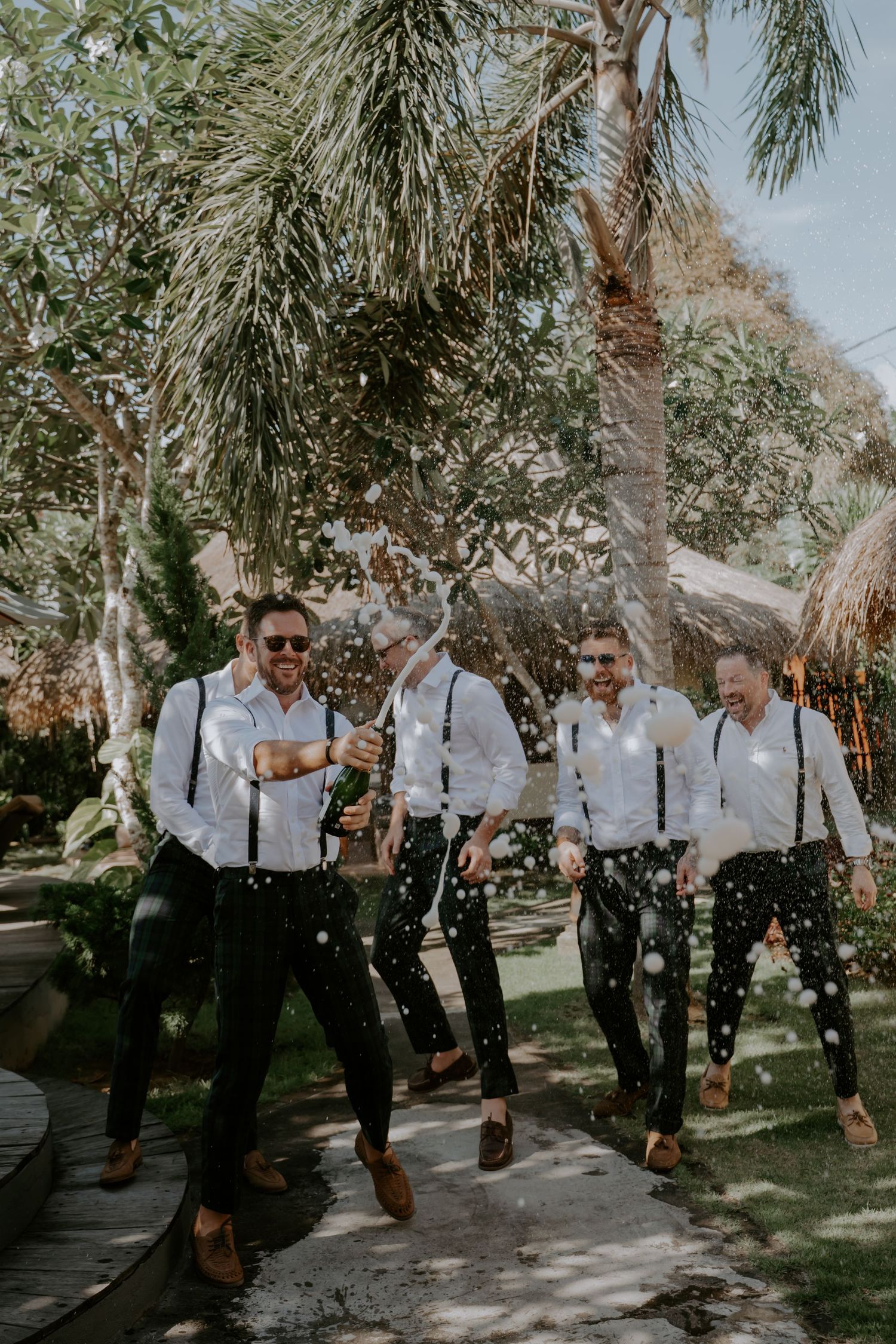 A group in black and white attire poses playfully under palm trees during an outdoor celebration.