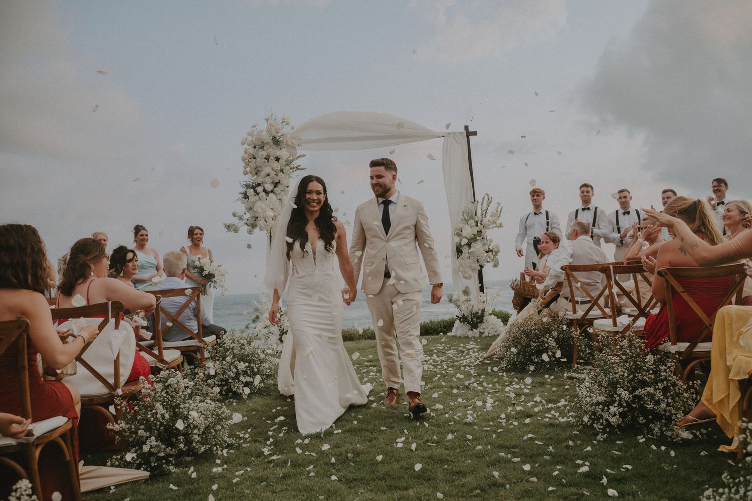 Wedding guests celebrate with confetti during an outdoor ceremony against a scenic mountain backdrop.