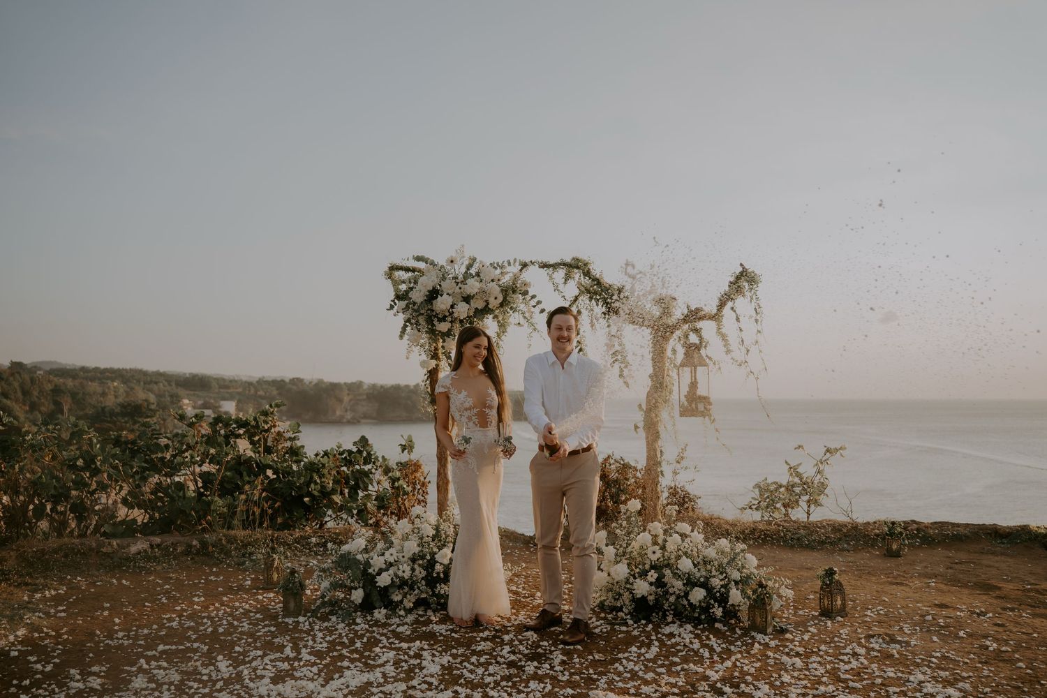 A romantic beach wedding ceremony setup with dried palm leaves and floral arrangements at sunset.