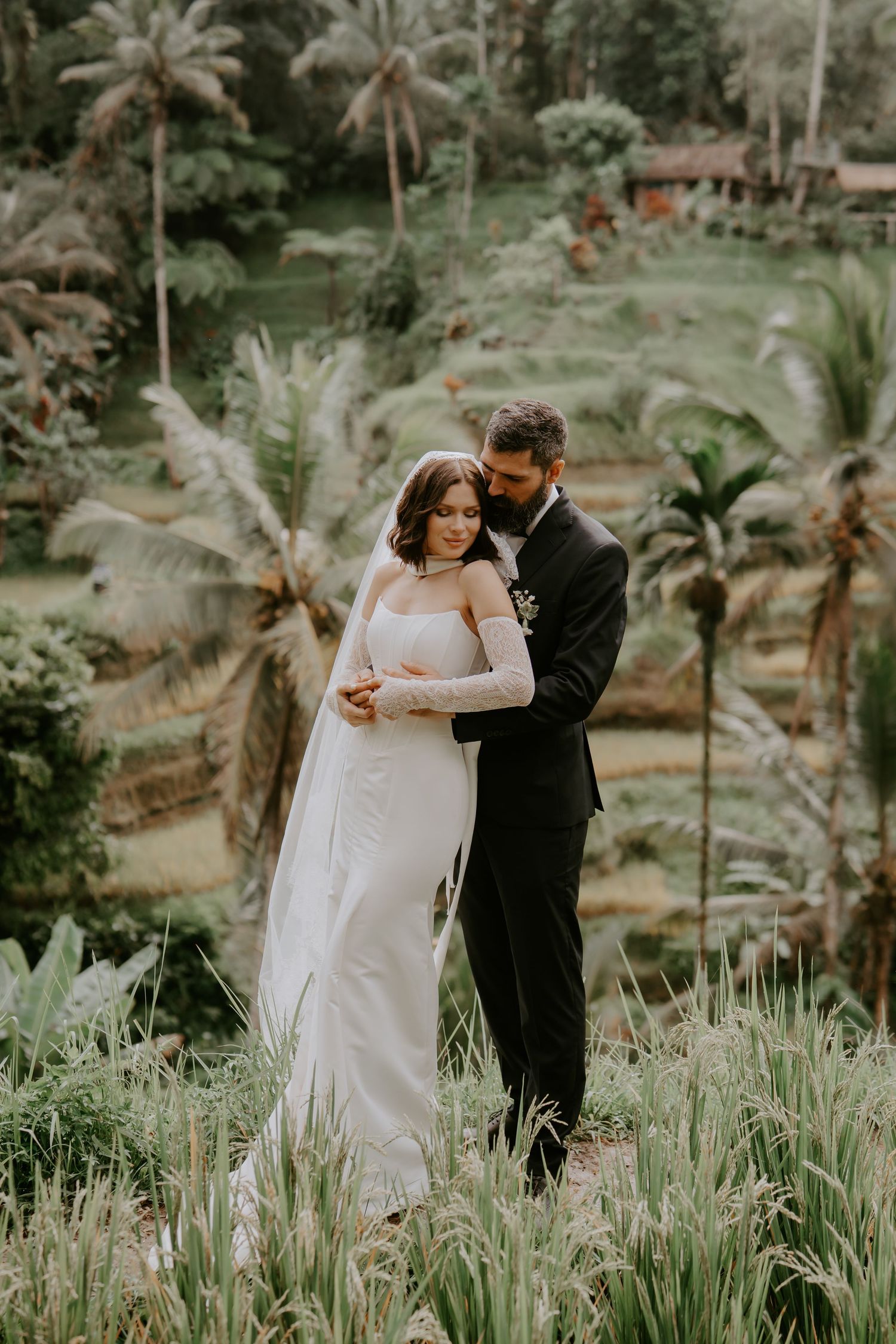 A couple shares an intimate dance moment surrounded by lush tropical greenery and palm trees in a garden setting.