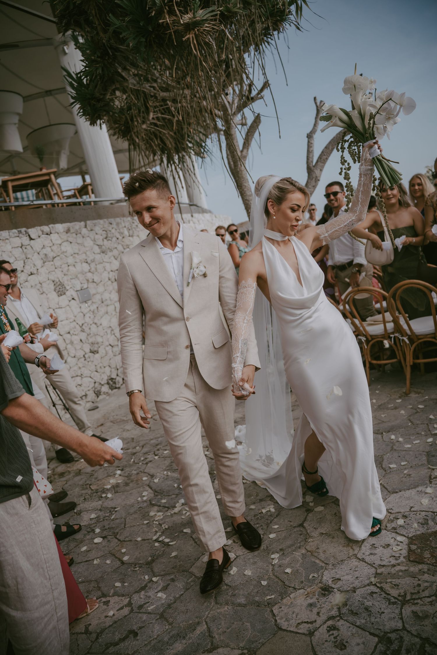 Newlyweds walking hand in hand on stone pathway after their beachside ceremony.
