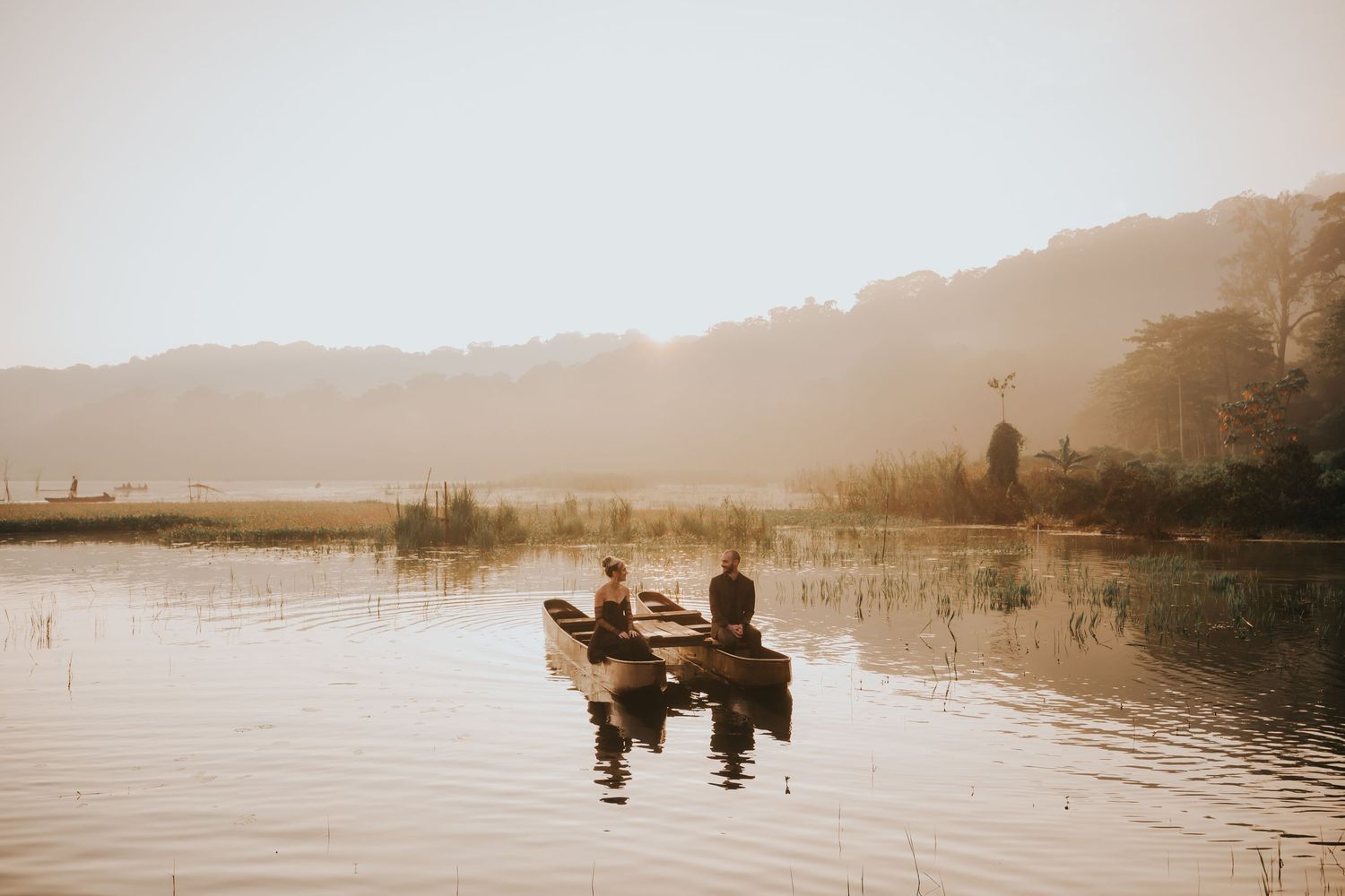 Silhouetted figures stand by a misty lake during sunset creating a romantic atmospheric scene.