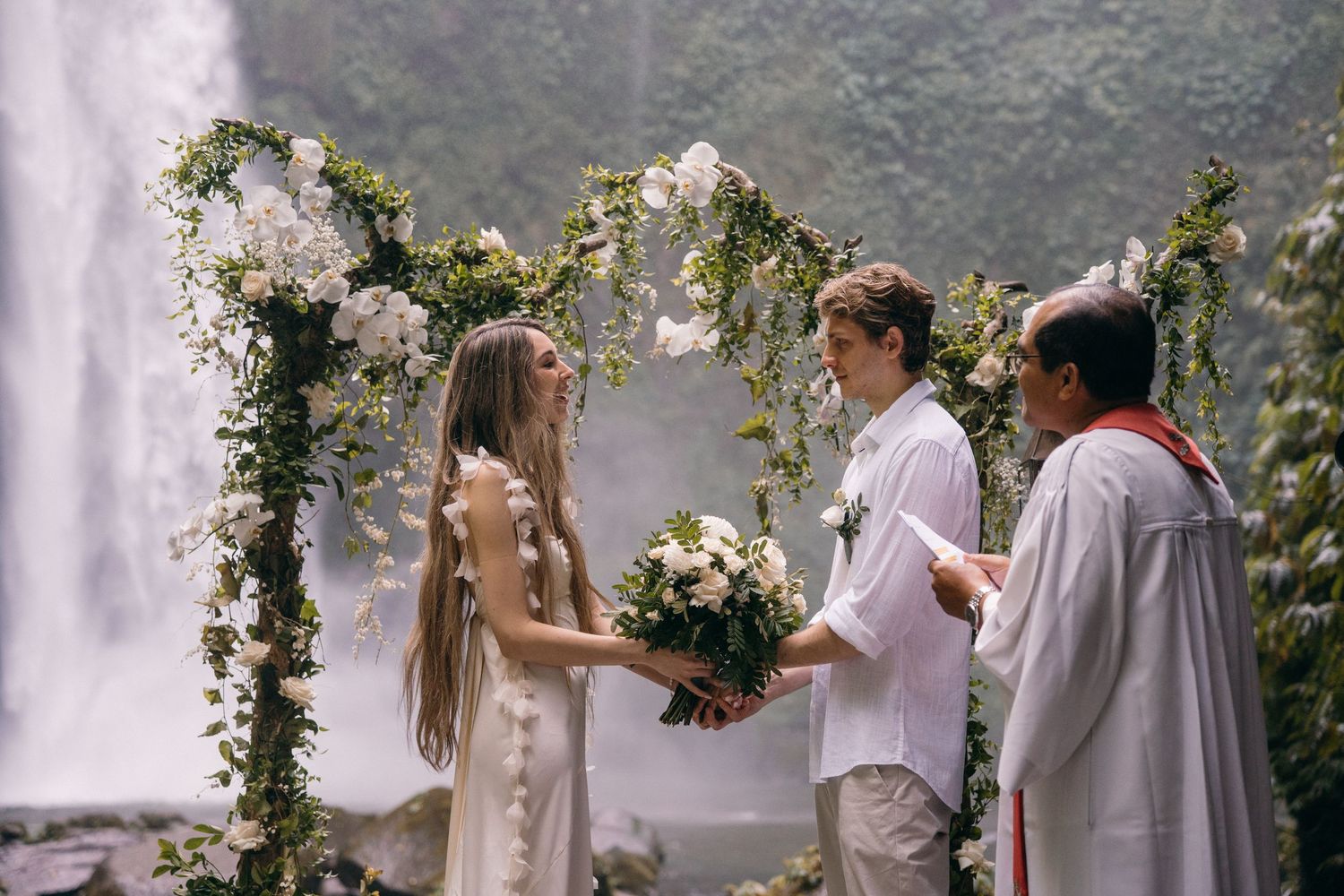 Romantic outdoor wedding ceremony under floral arch with guests watching the couple exchange vows.